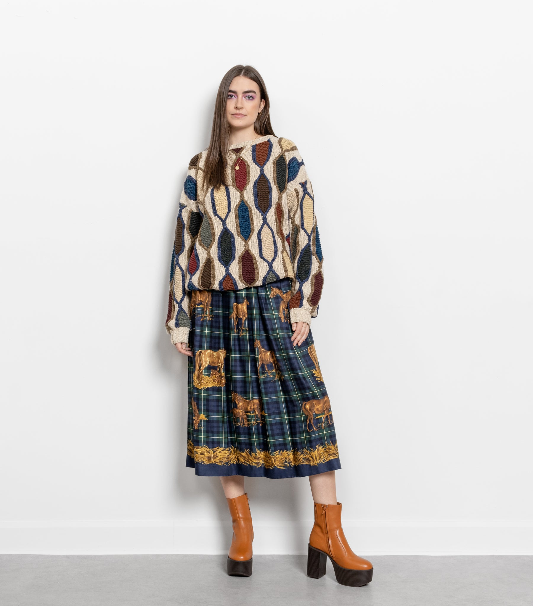 Woman wearing a patterned sweater and plaid skirt with brown boots on a white background