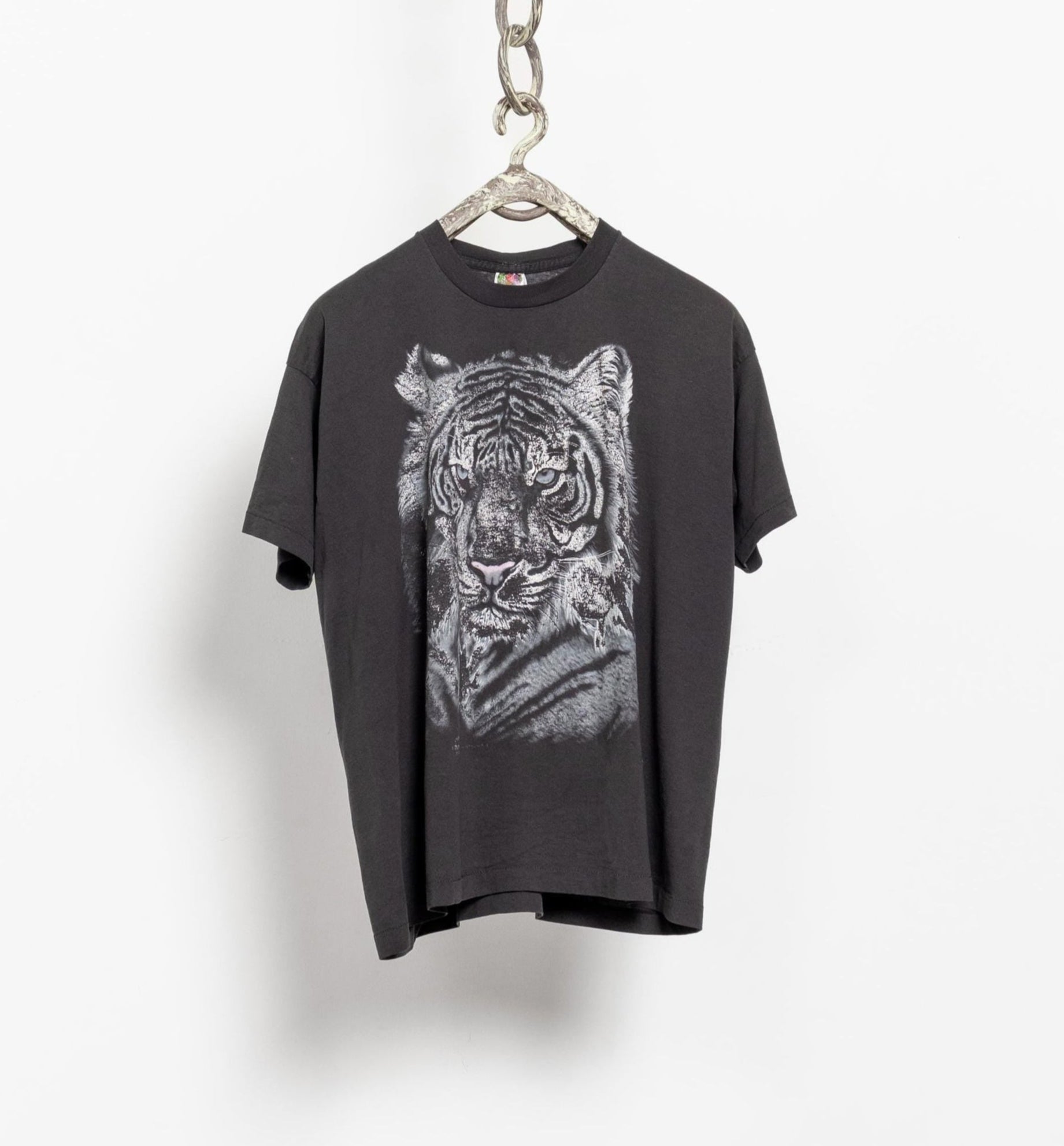 A vintage white tiger short sleeve tee hanging on a chain, with a graphic of a tiger on the front in faded black and gray colors.