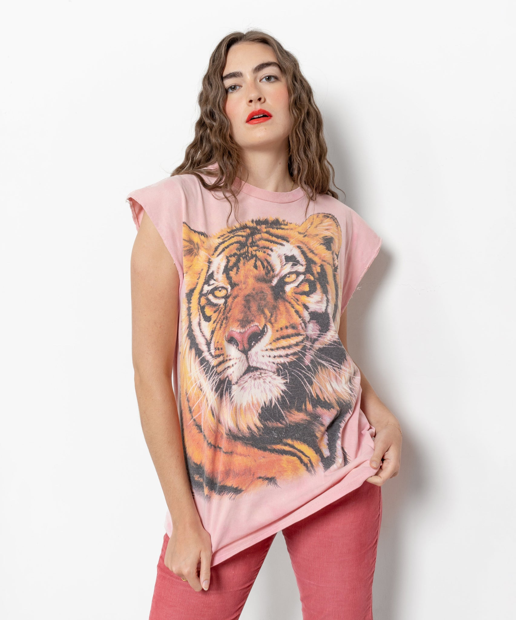 A person wearing a pink sleeveless t-shirt with a large tiger graphic in the center, the shirt has raw edge cut off sleeves with some fraying and a small amount of paint splatter near the bottom hem on the back.