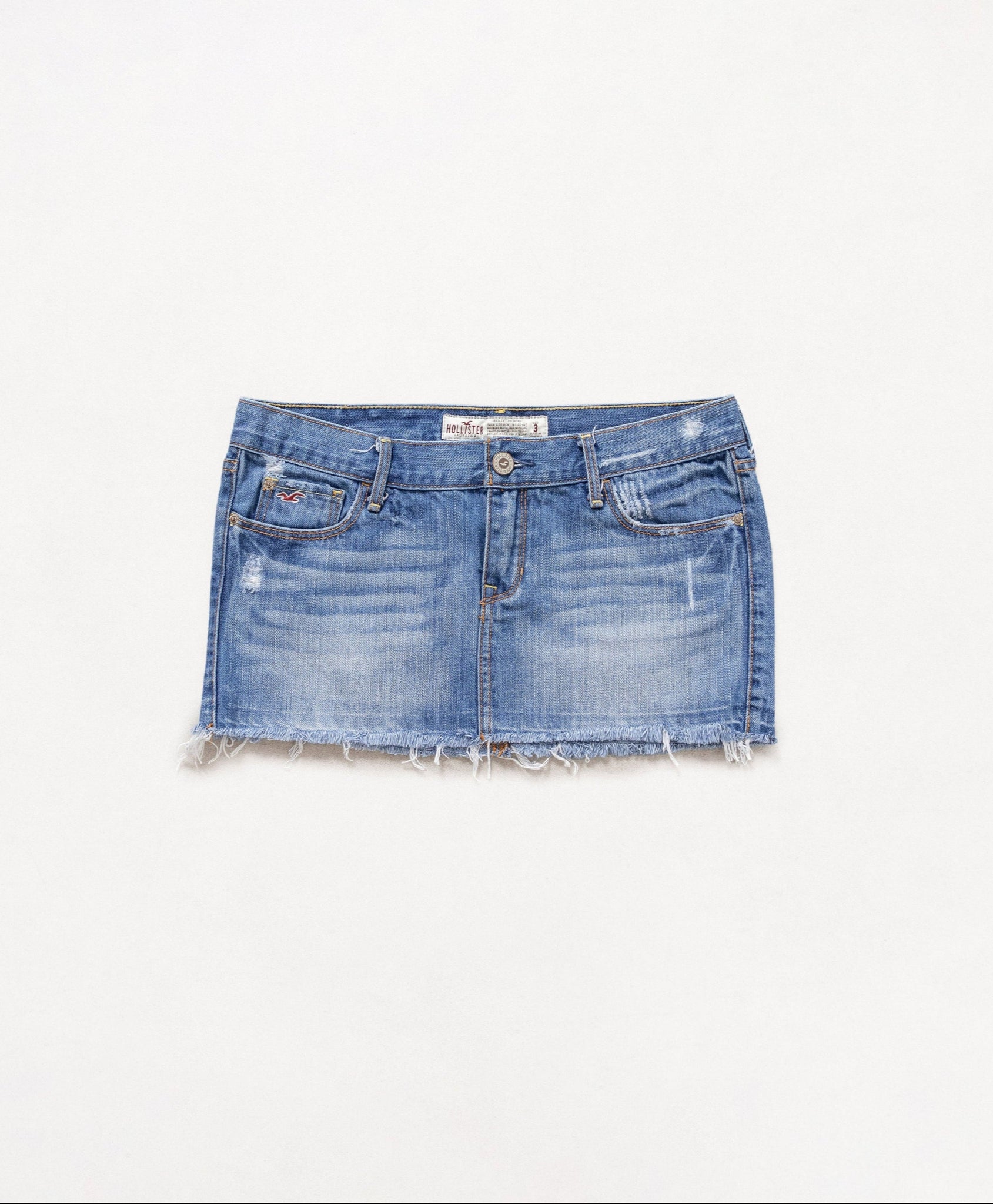 A vintage 2000's ultra low rise denim mini skirt with a faded design and raw bottom hem, displayed on a white background.