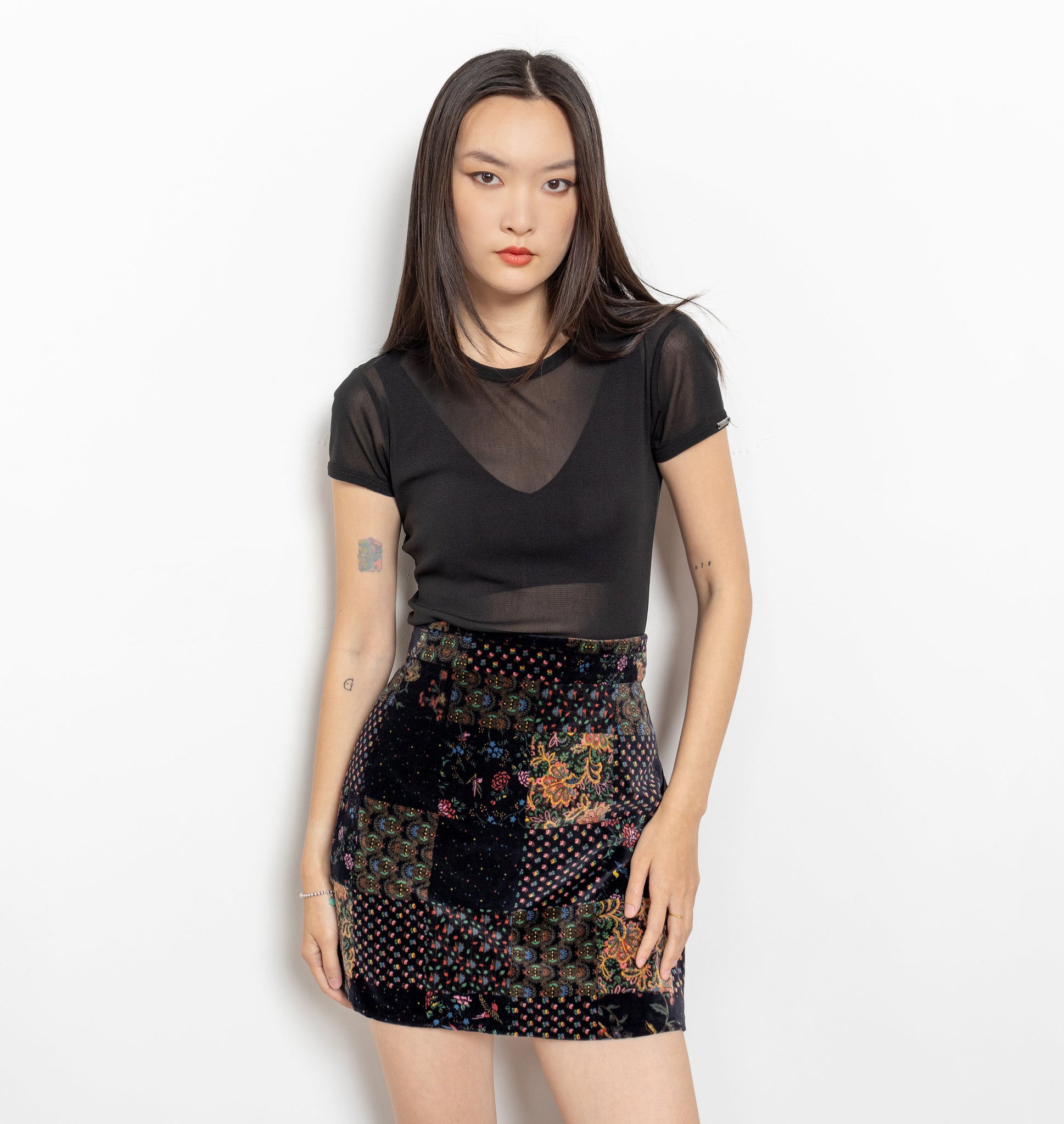A person wearing a vintage 90's patchwork print velvet mini skirt with a high waist pencil skirt fit, zipper on the side, and appears unlined.