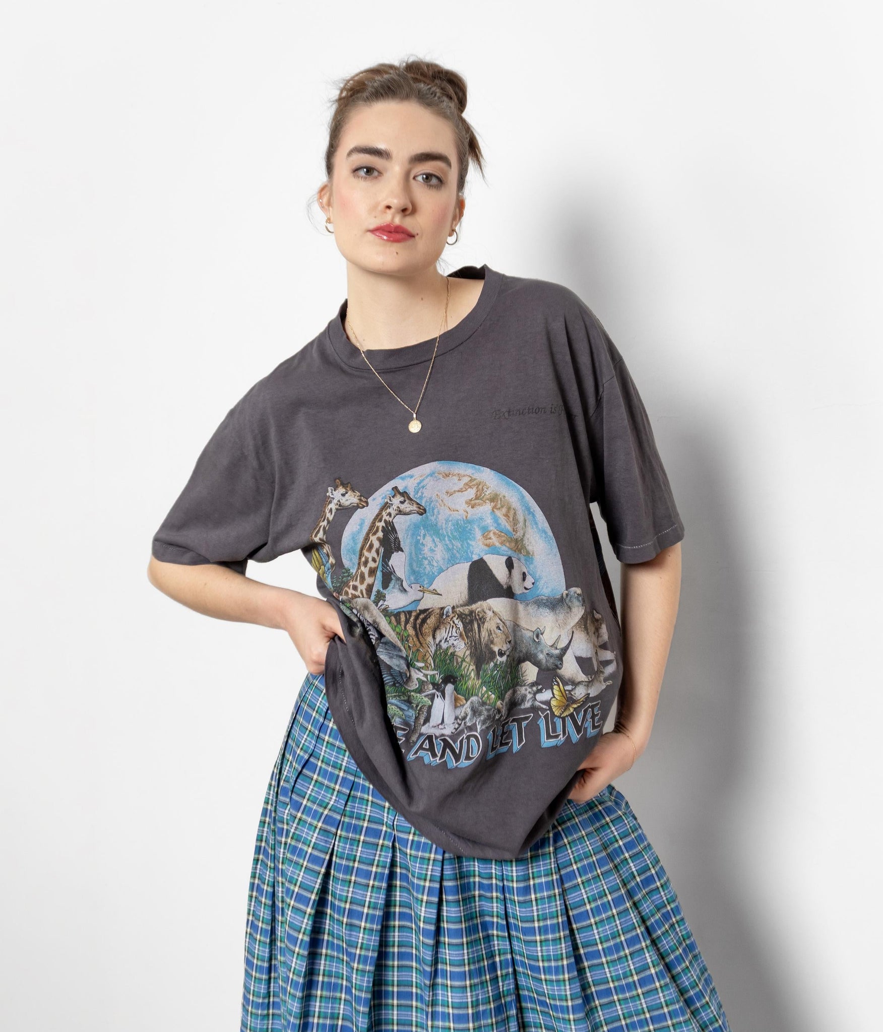 Person wearing a graphic t-shirt with a design and plaid skirt on a plain background