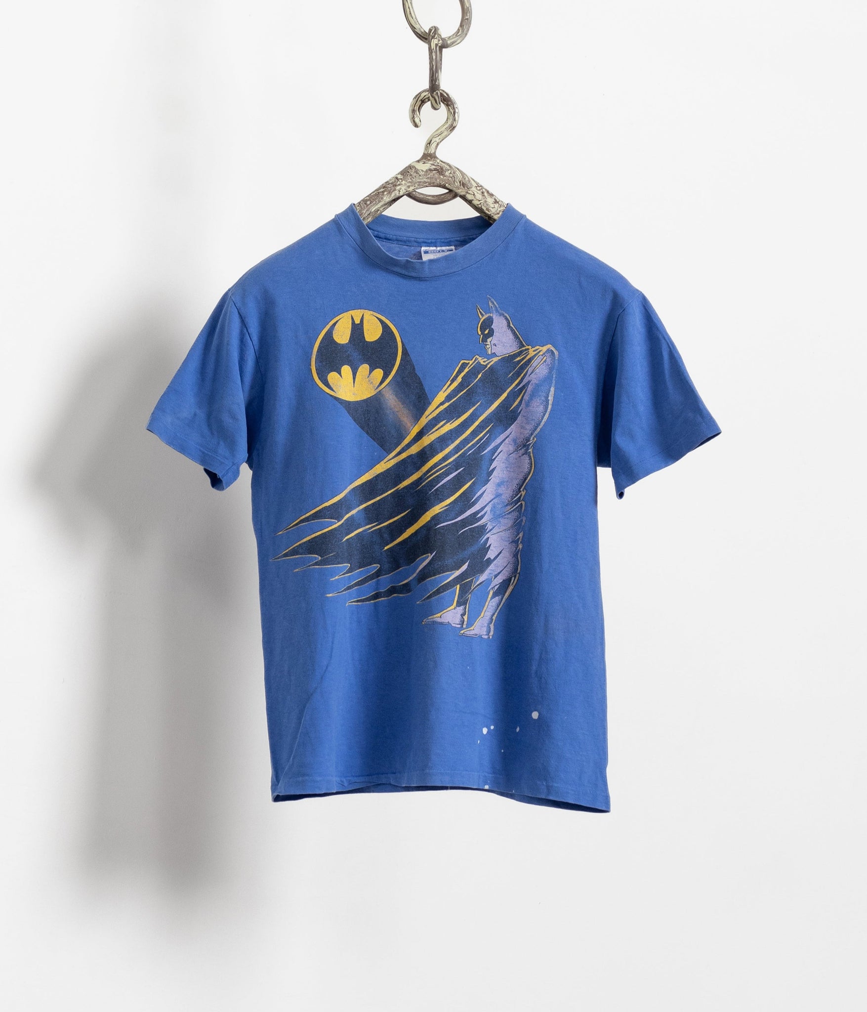 A vintage blue Hanes Beefy Tee with a graphic of the Batman character in a yellow and black design, displayed on a hanger against a white background.