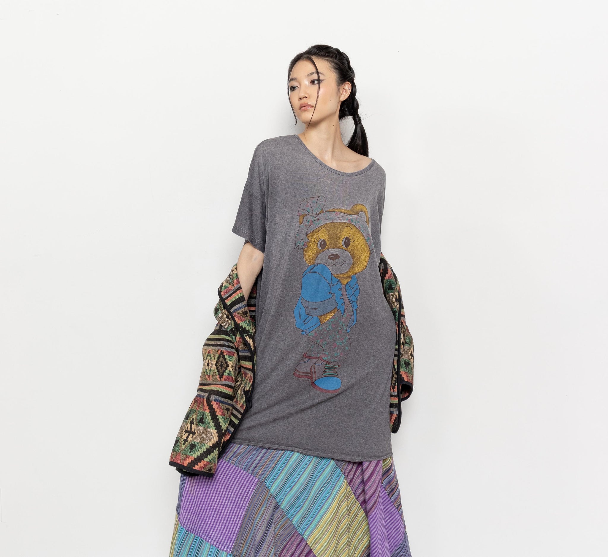 Person wearing a gray t-shirt with a bear graphic and a colorful patterned jacket on a white background