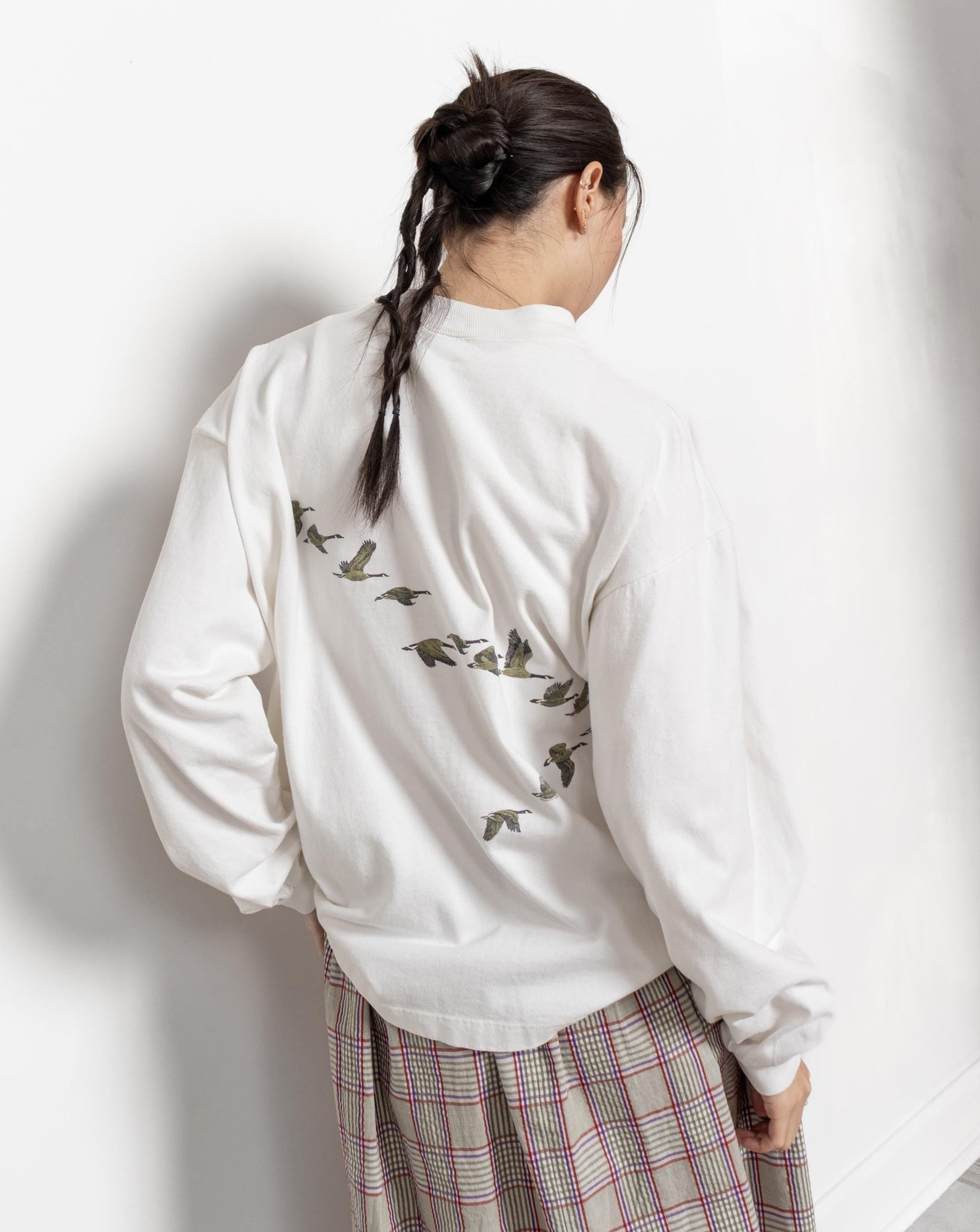Person wearing a white sweatshirt with bird designs and plaid pants on a light background