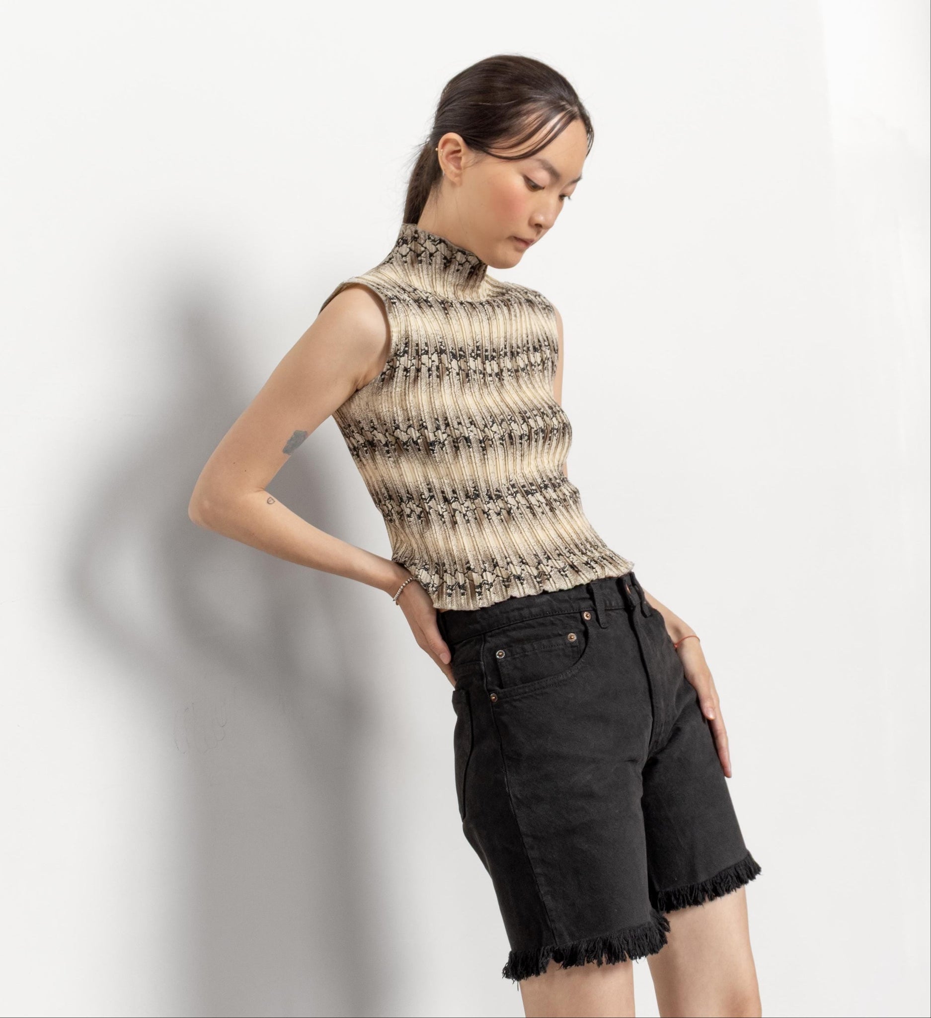 Woman wearing a sleeveless patterned top and black shorts against a white background