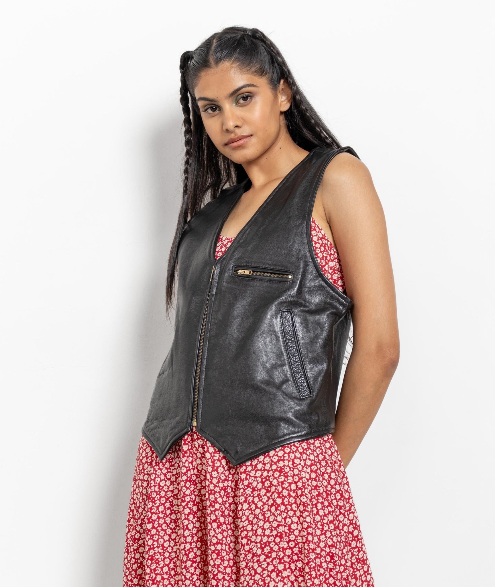 Woman wearing a black leather vest over a red floral dress on a white background