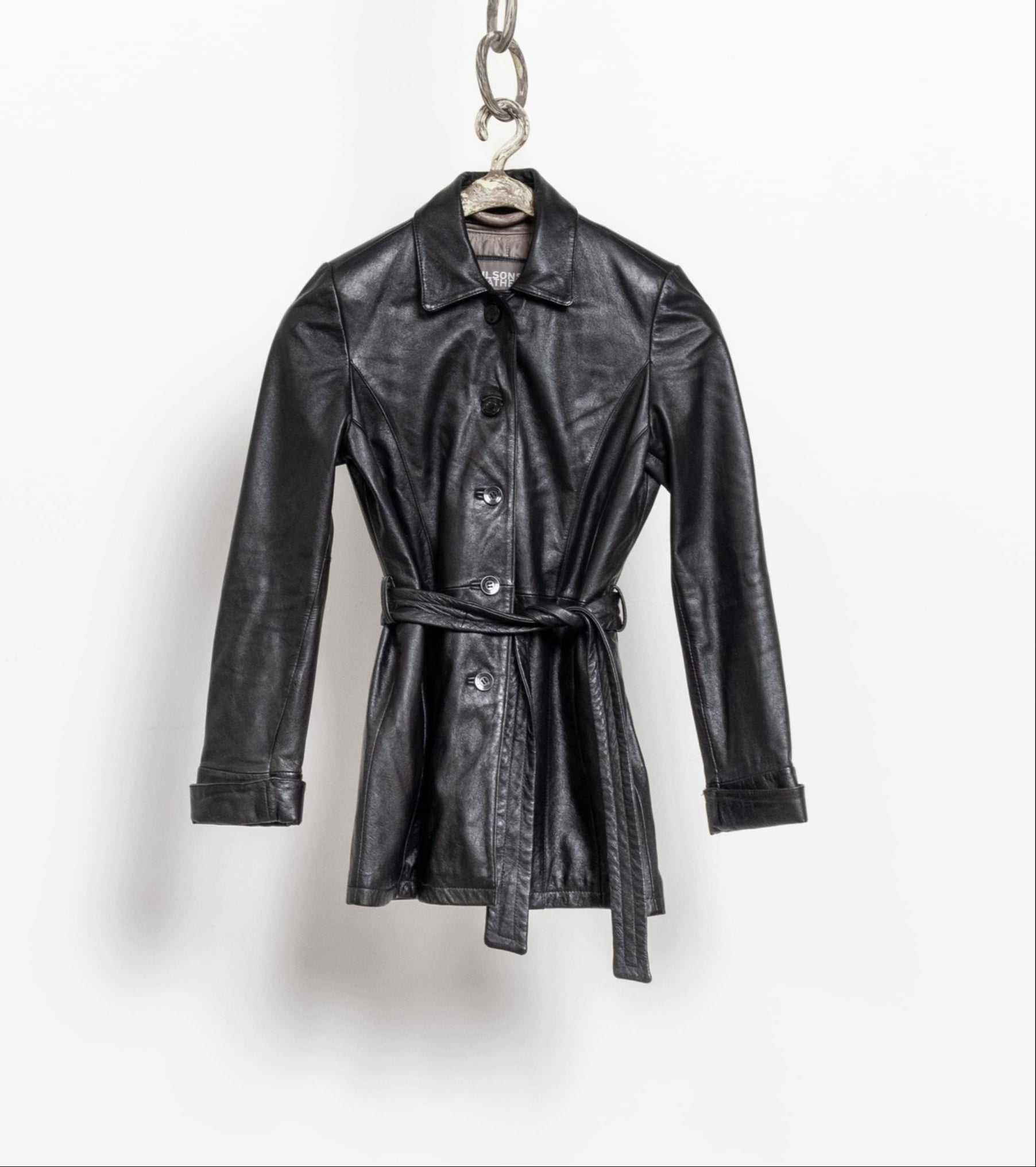 Black leather trench coat on a hanger against a white background