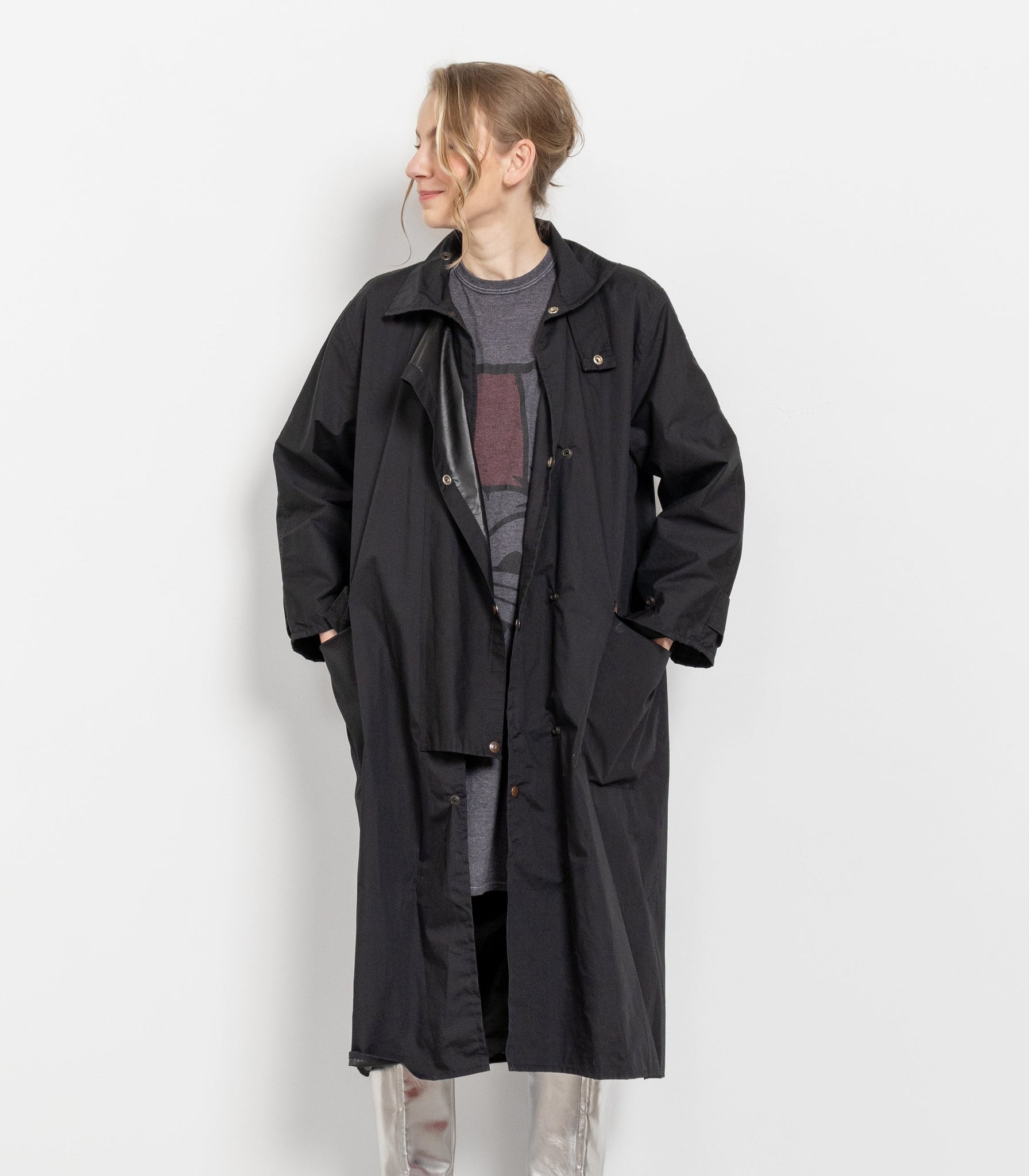 Person wearing a long black coat and silver boots against a white background