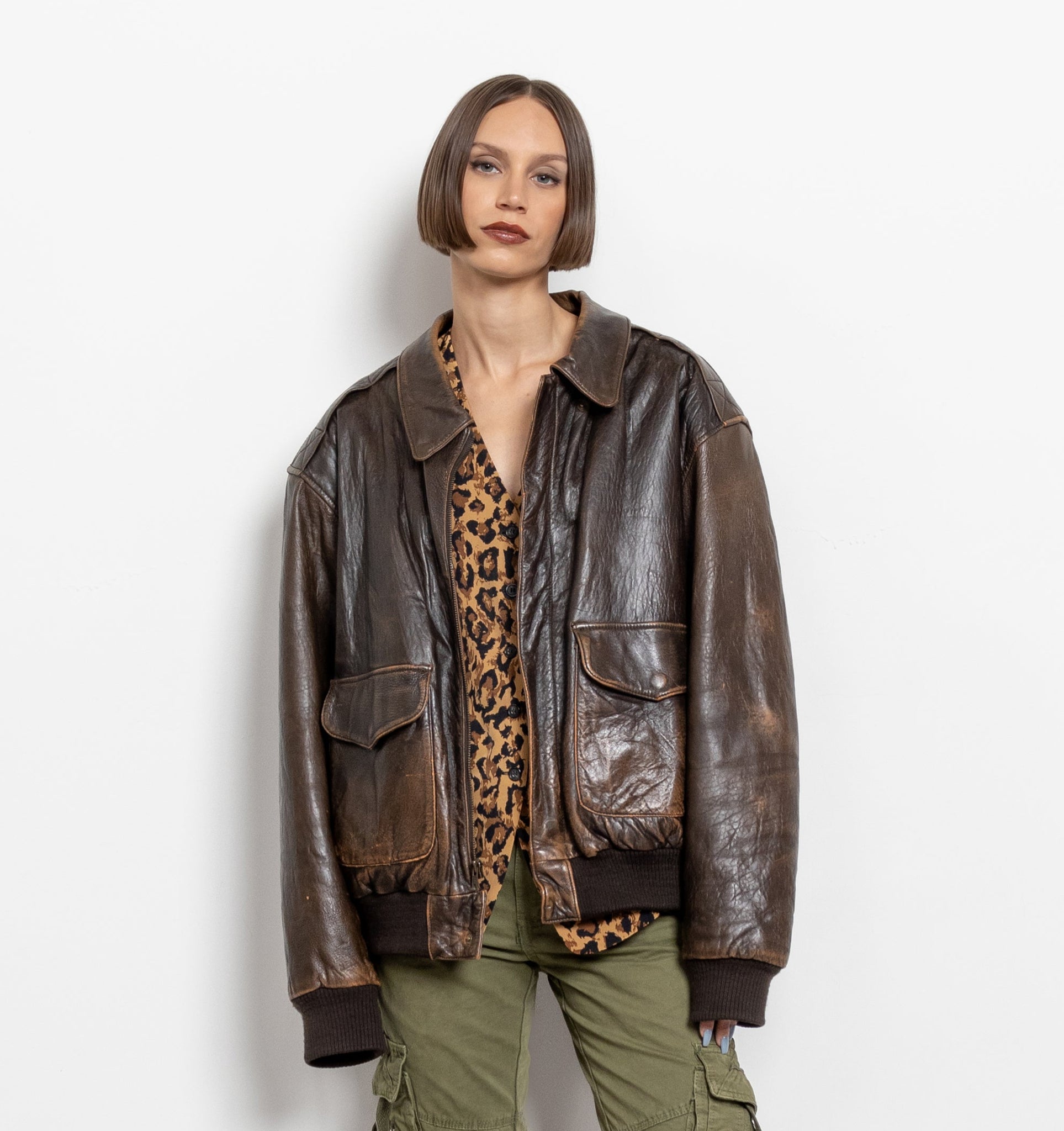 Person wearing a brown leather jacket, green cargo pants, and brown platform boots on a white background