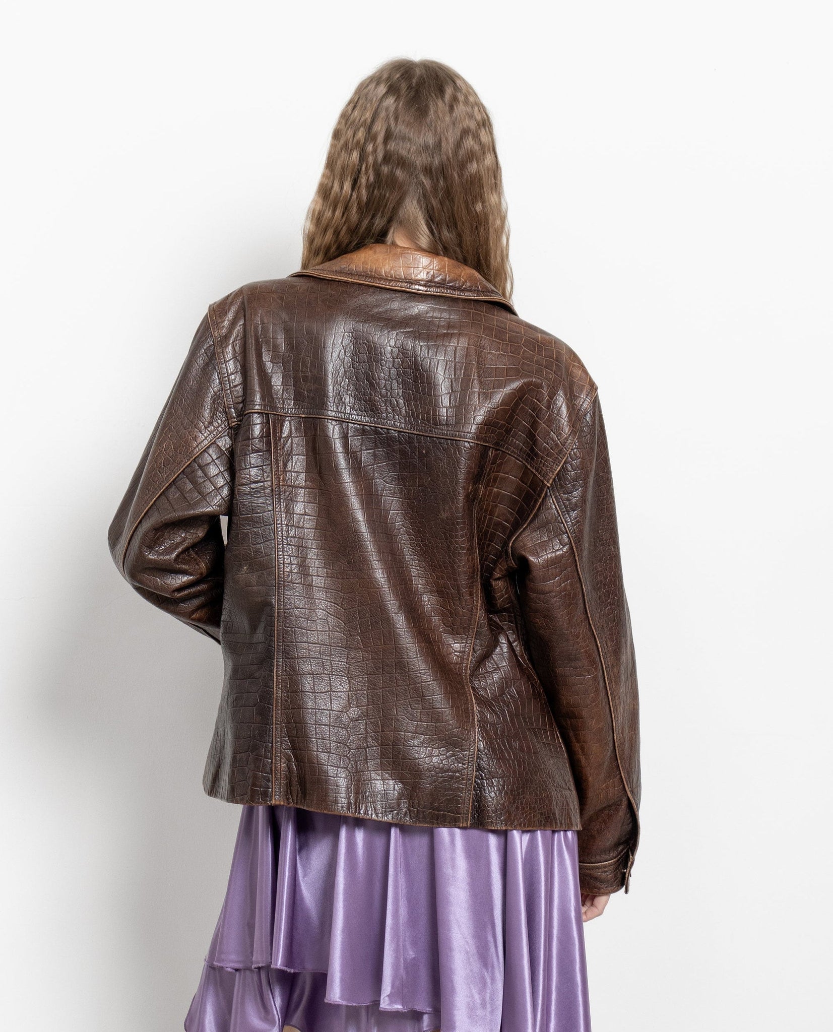 Person wearing a brown leather jacket and purple dress on a white background
