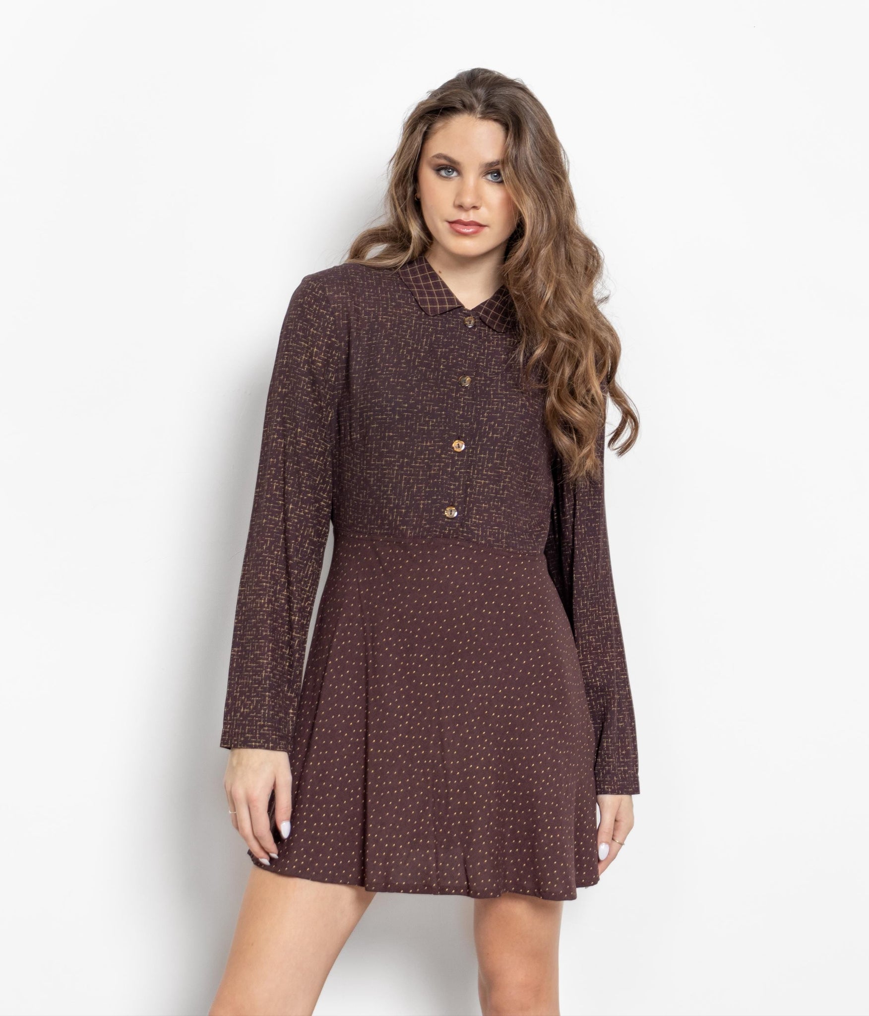 A woman modeling a vintage 90's brown polka dot print long sleeve collared mini dress with a button-up bodice and a shorter skirt.
