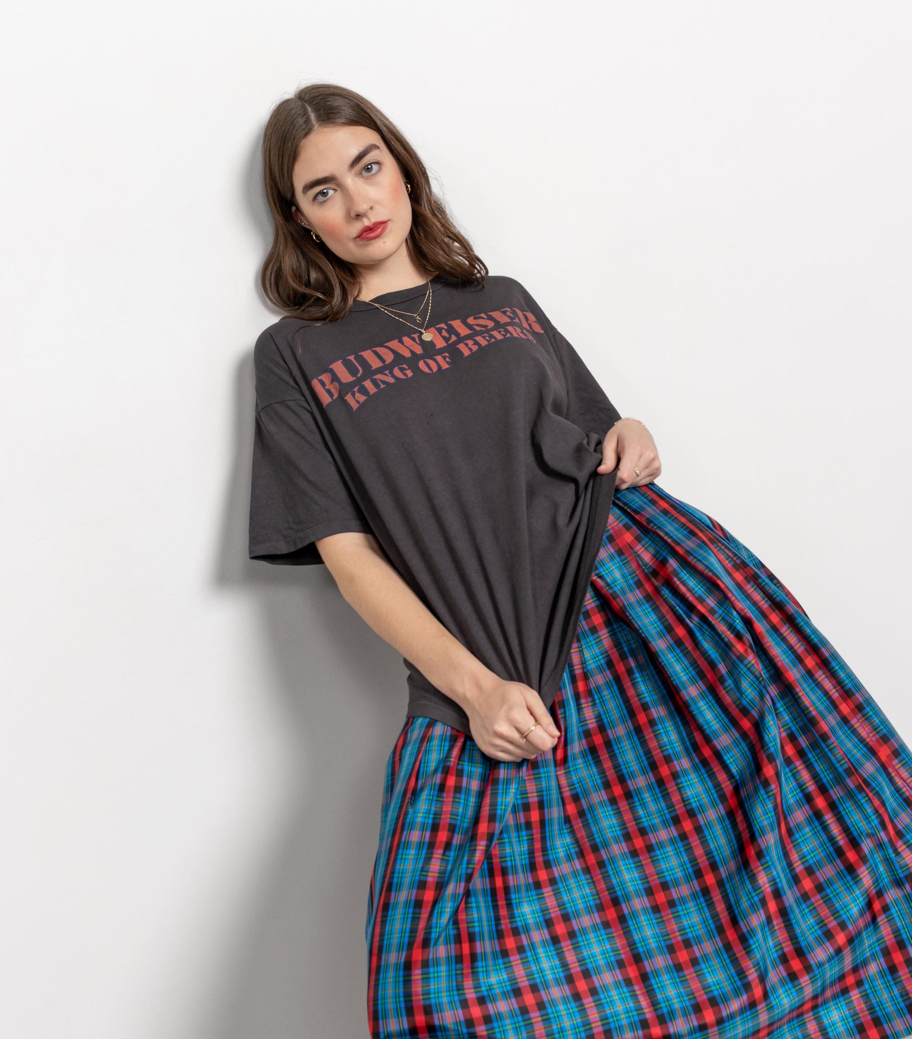 Woman wearing a dark gray t-shirt with text and a blue plaid skirt on a white background