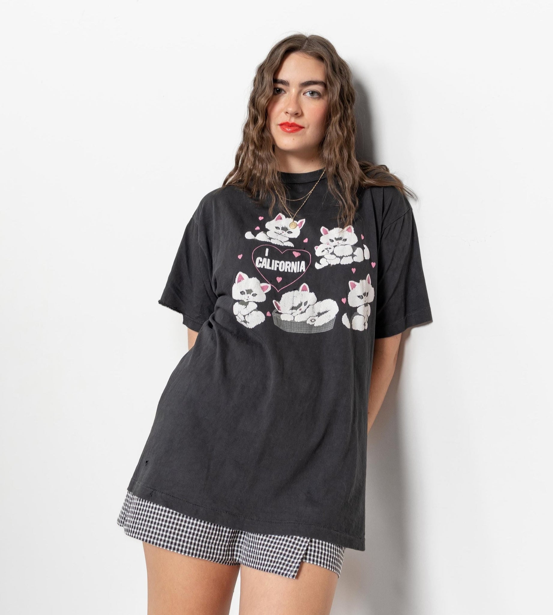A person wearing a vintage black t-shirt with a graphic design of cats and the text 'CALIFORNIA', paired with short shorts.