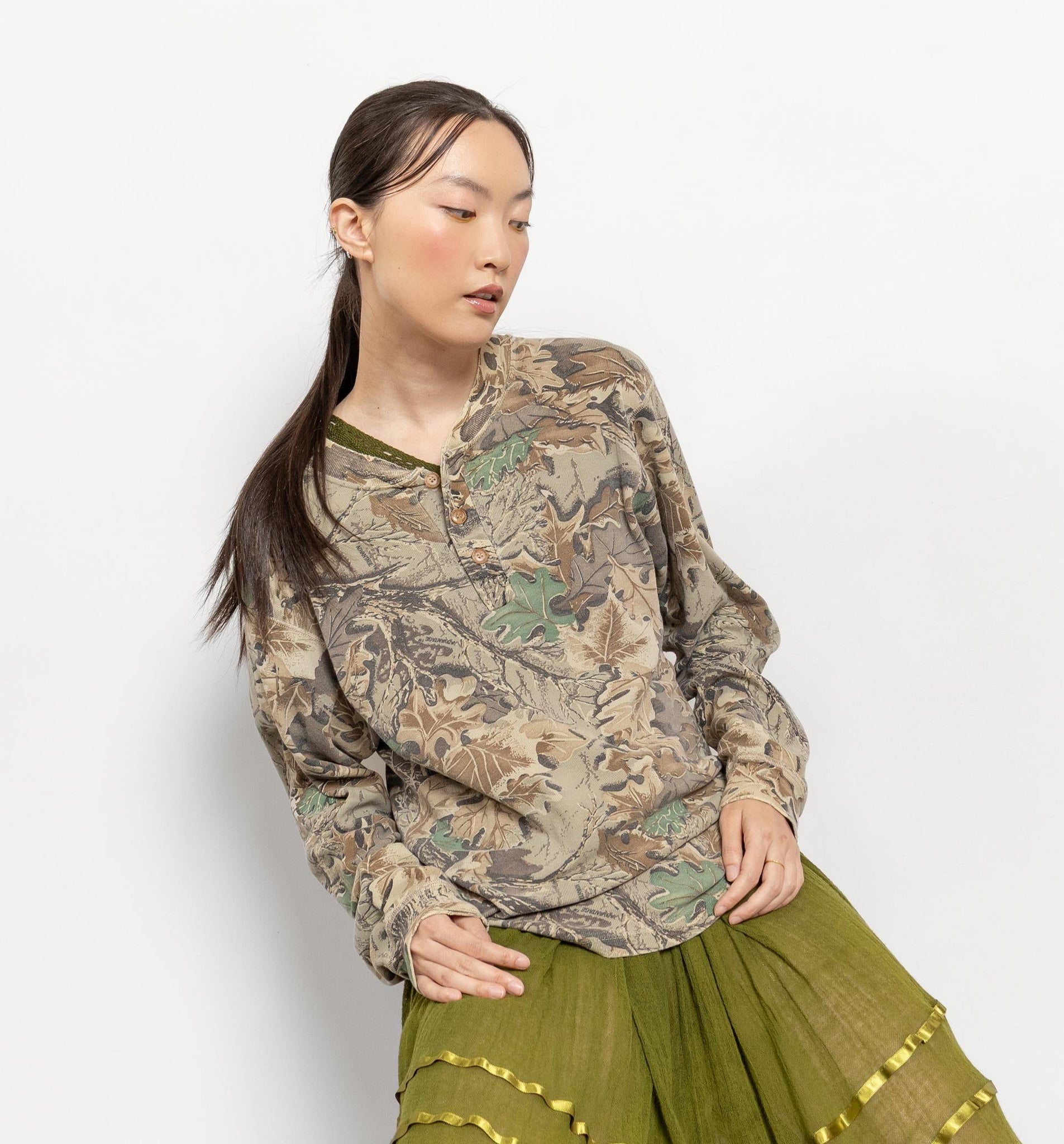 Woman wearing a patterned shirt and green skirt with gold accents on a white background