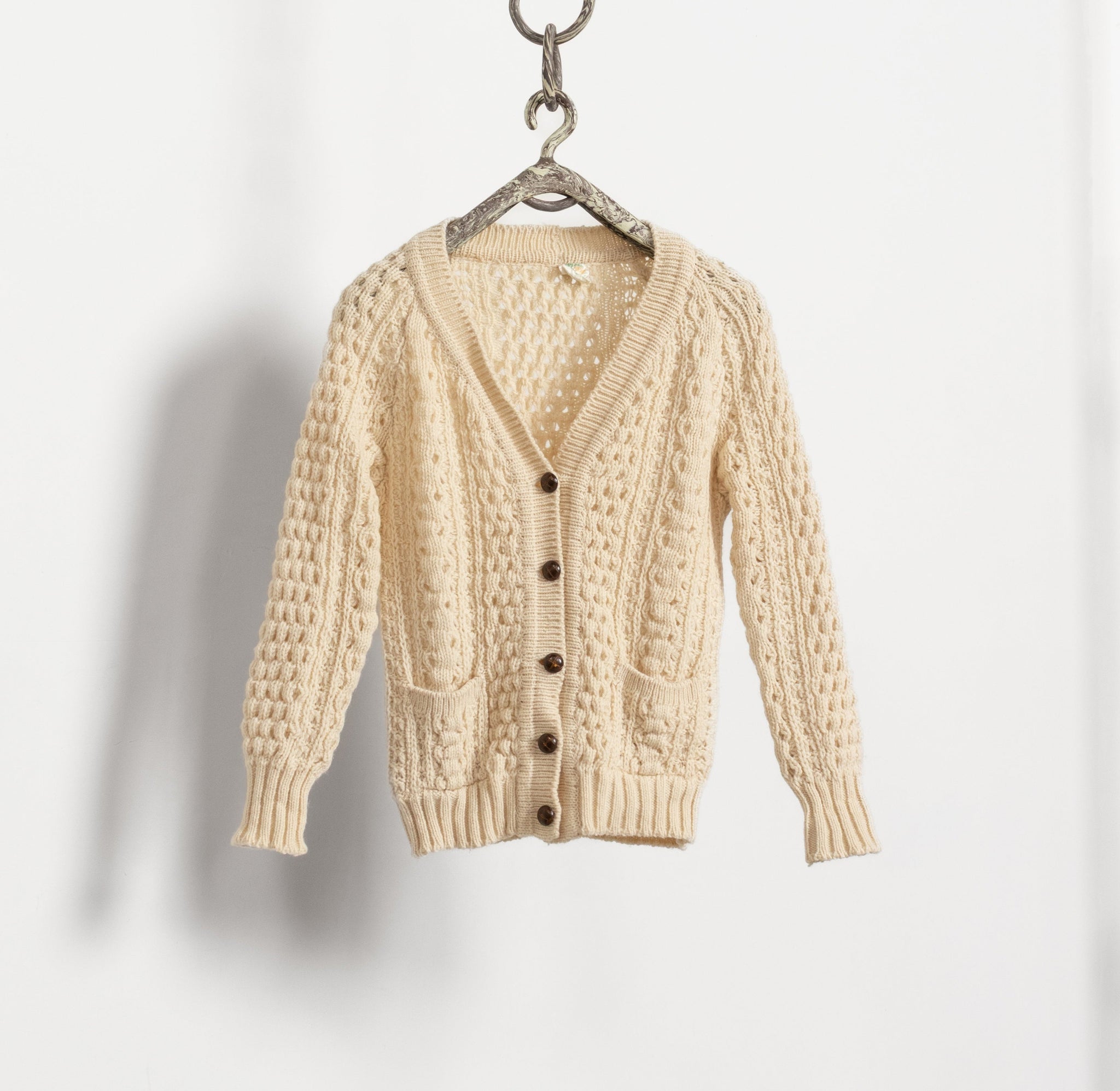 Beige cardigan hanging on a hanger against a light gray background