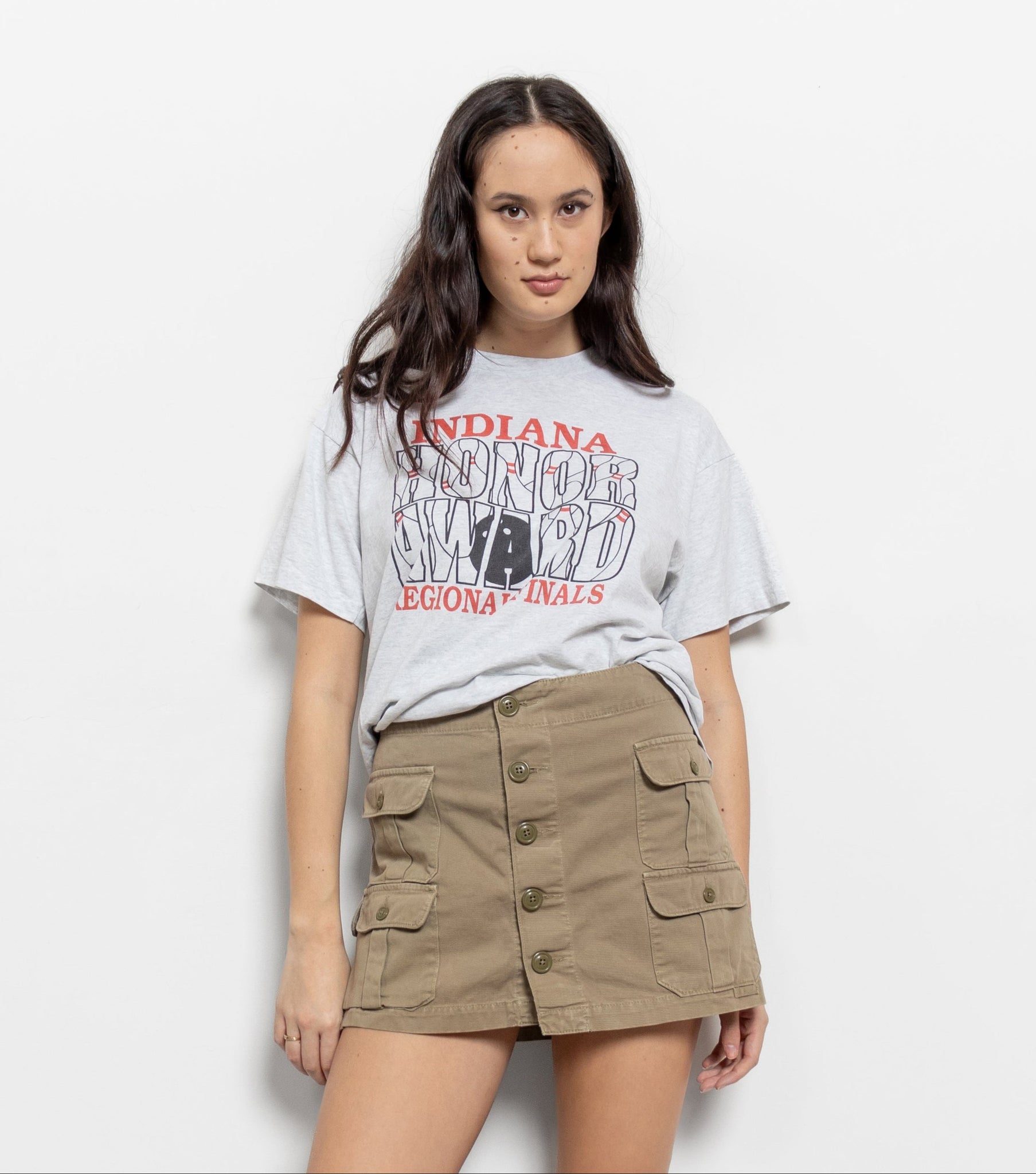 Woman wearing a graphic t-shirt and beige skirt on a white background