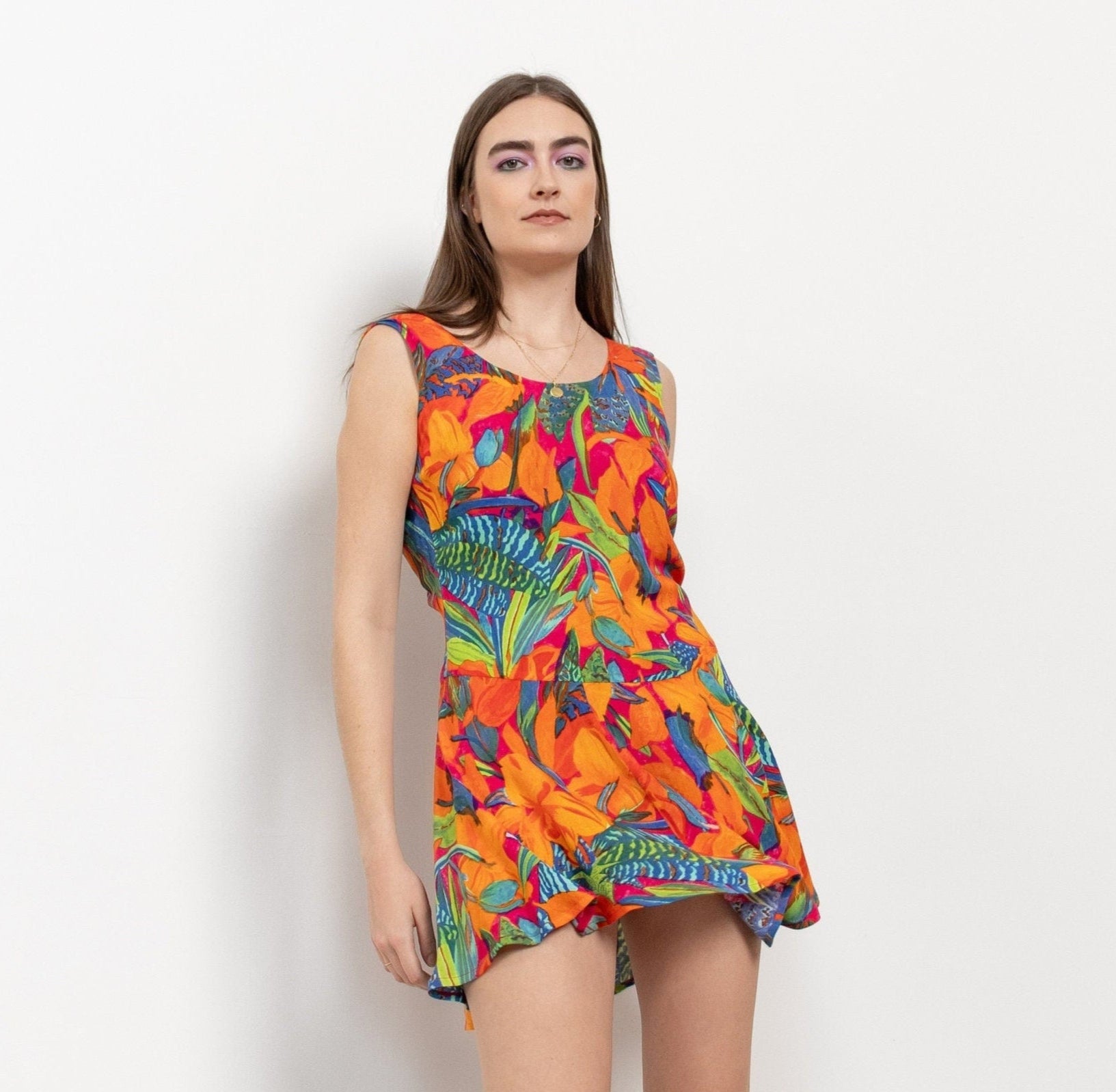 A woman modeling a vibrant, multicolored floral mini dress with a scooped neckline and black boots.