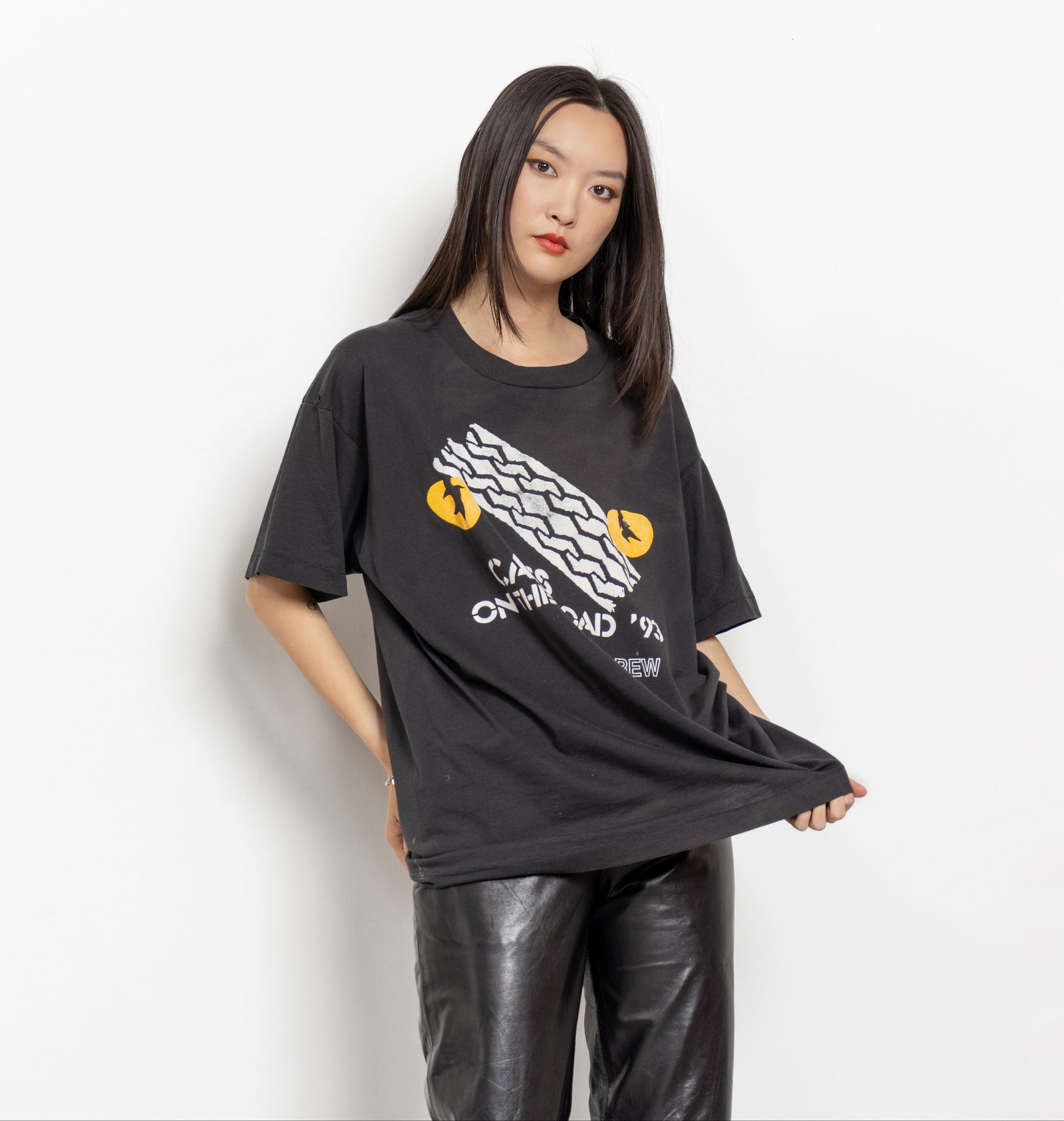 A person wearing a black t-shirt with a graphic print of cats and the text 'Cats on the Road' on the front, paired with black leather pants.