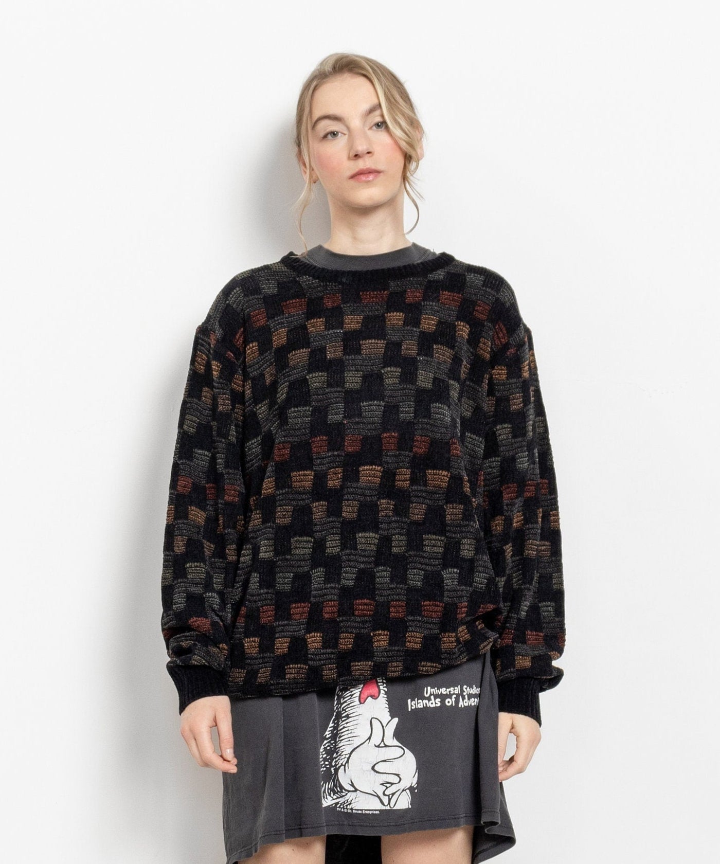 Person wearing a patterned sweater, black skirt with white text, and silver knee-high boots on a white background