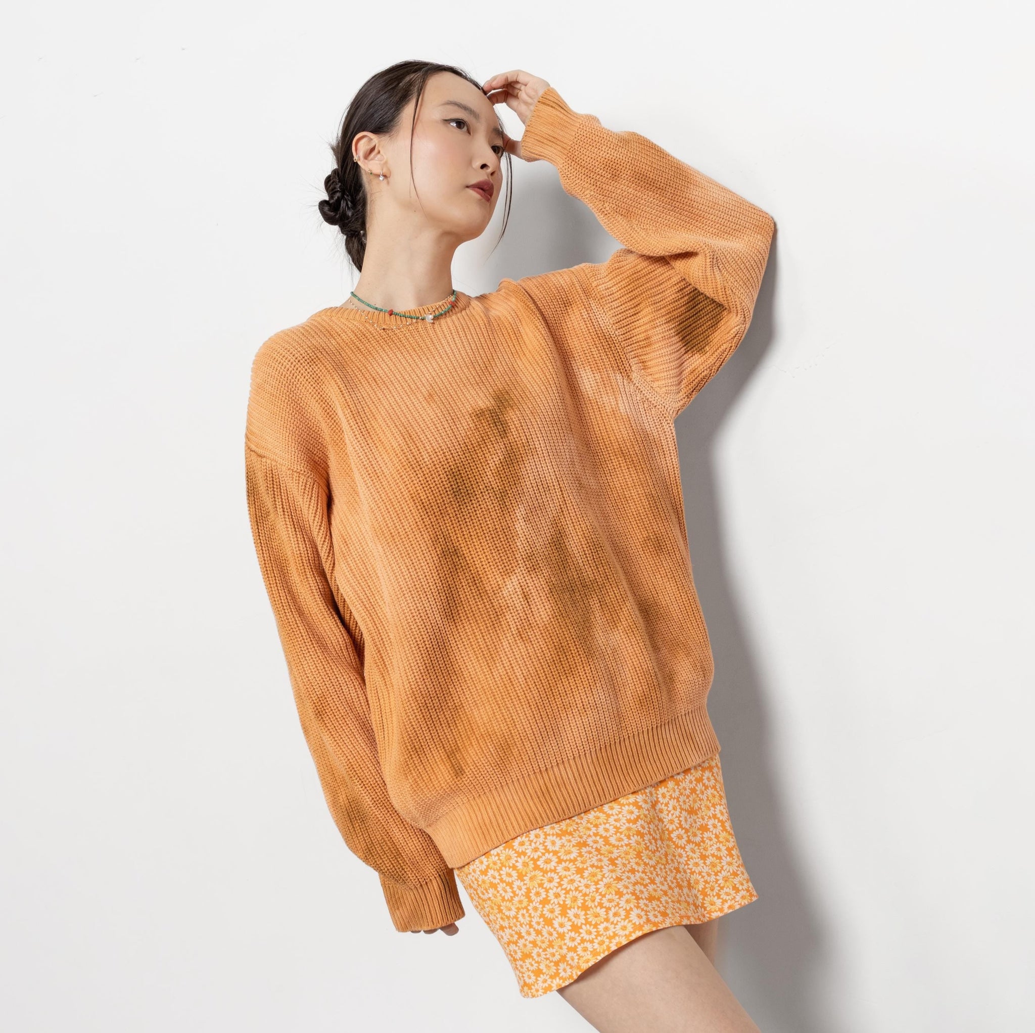 A person wearing an oversized vintage peach tie-dye sweater with a crew neck, paired with a short skirt.