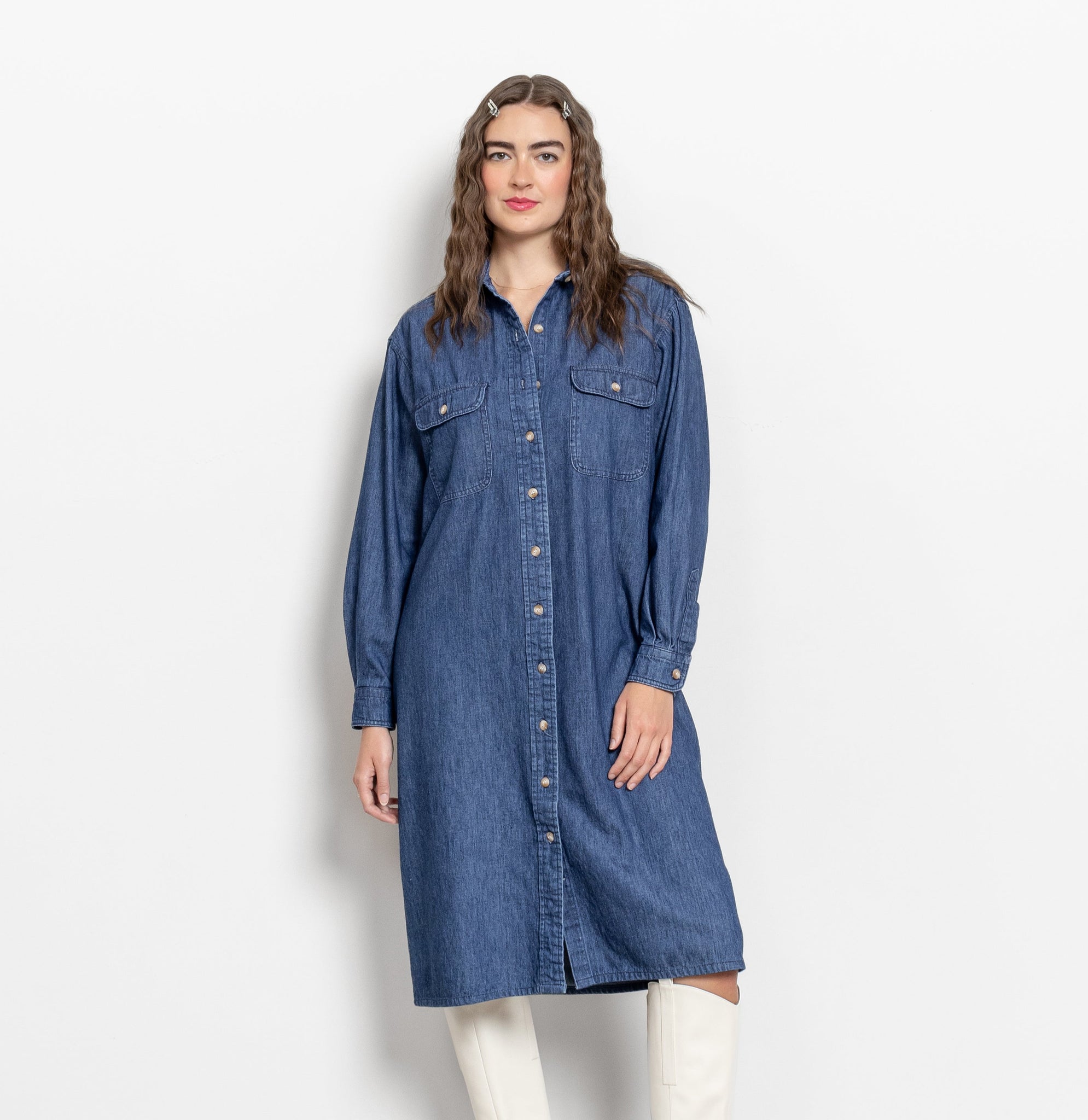 A woman modeling a long sleeve denim midi dress with buttons down the front, two side pockets, and a collar.