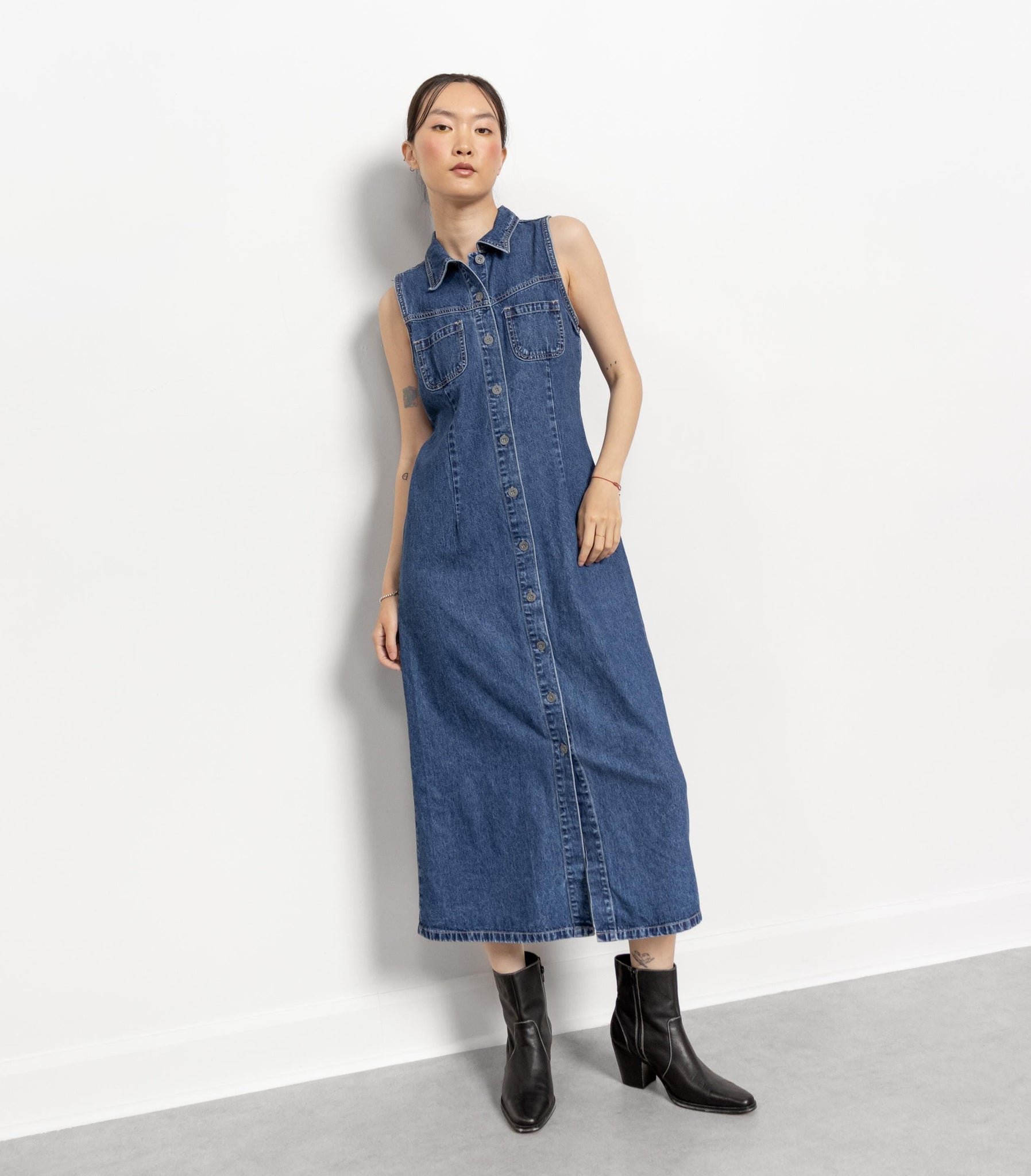 Woman wearing a blue denim dress with black boots on a white background