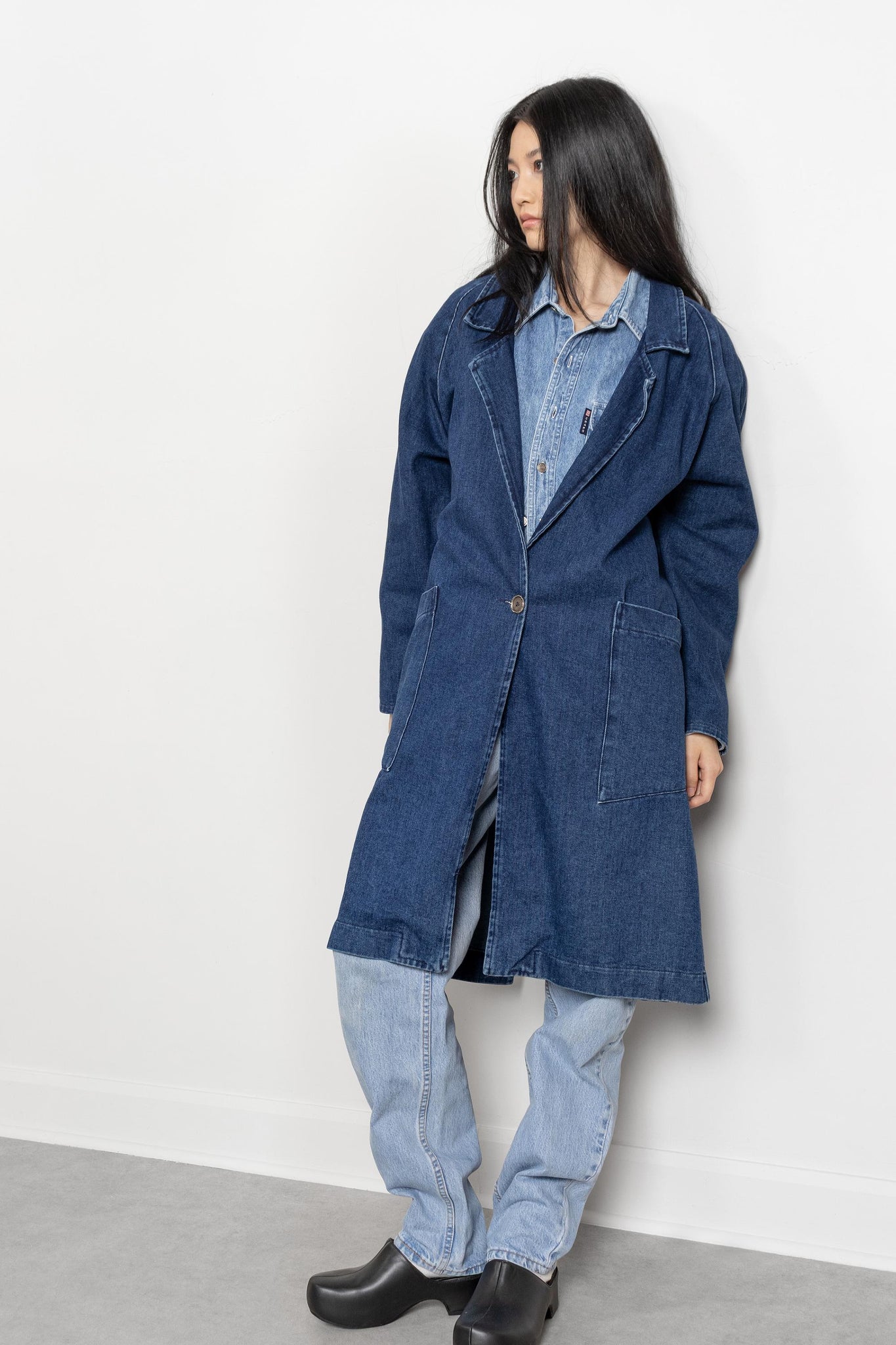 Person wearing a long blue denim coat against a white background