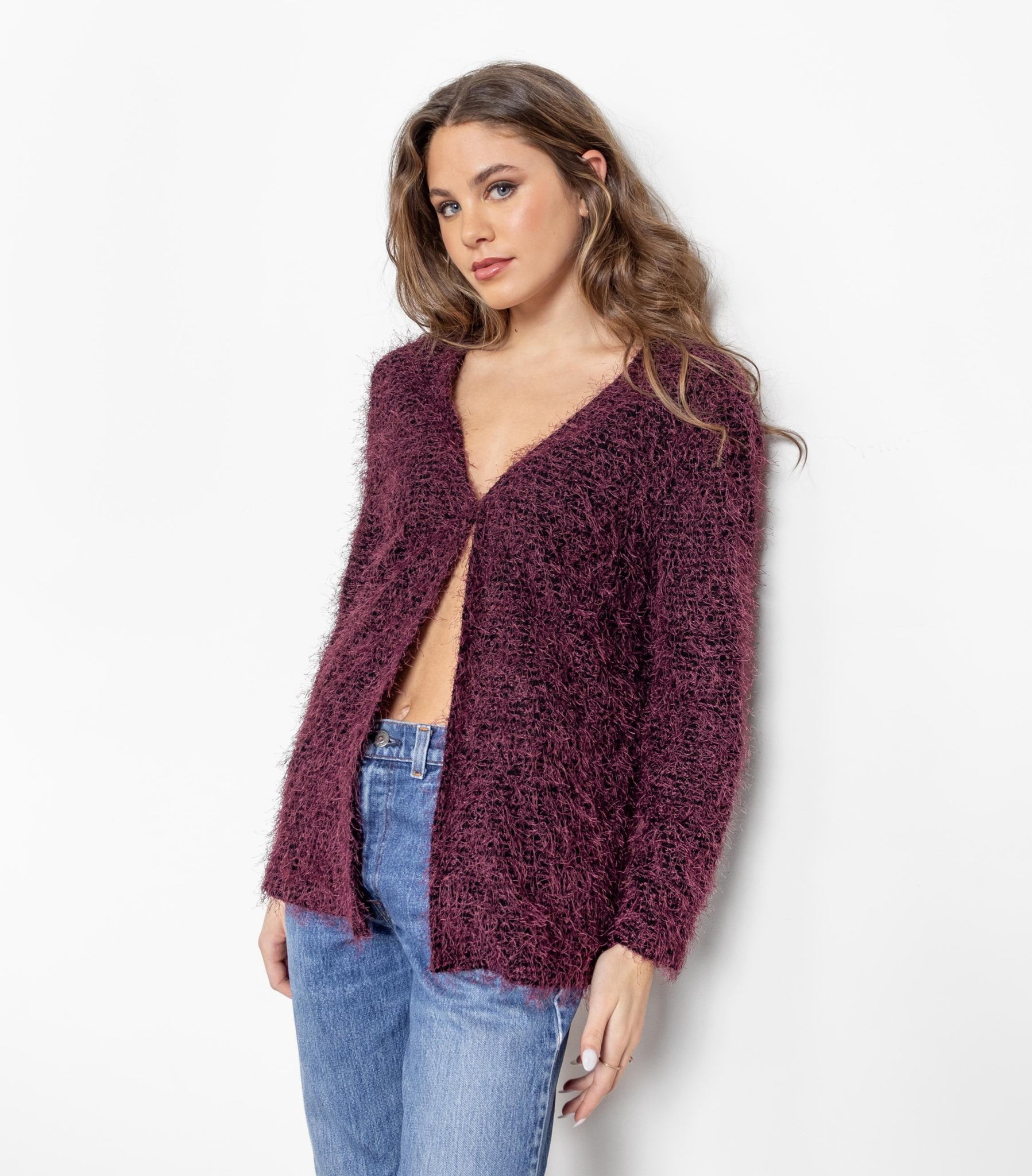 Woman wearing a burgundy cardigan over a black top with blue jeans on a white background