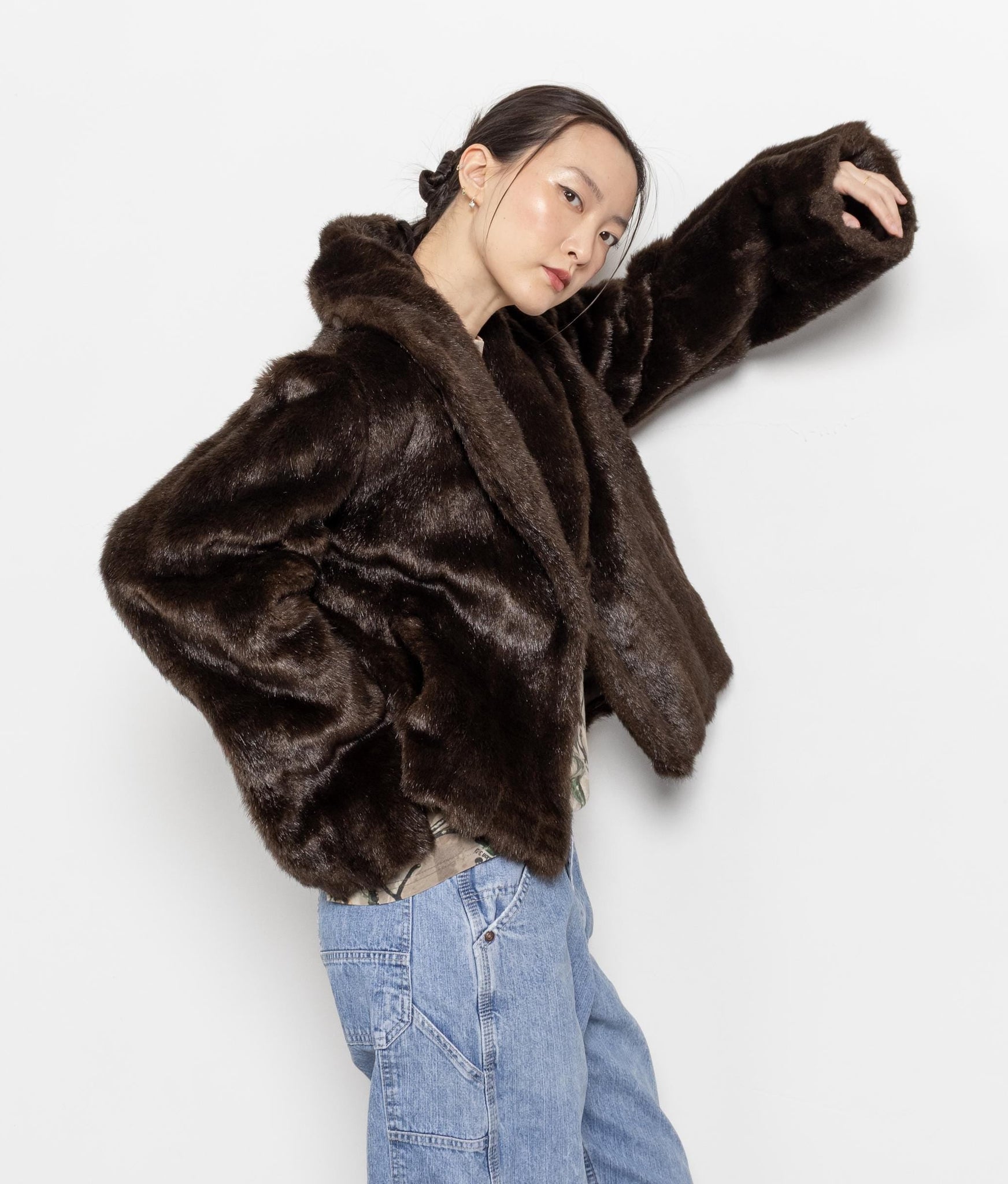 Person wearing a brown faux fur jacket and blue jeans on a white background