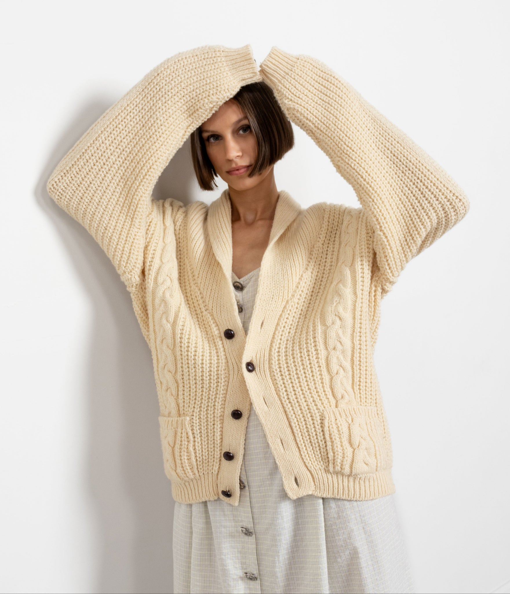 A woman wearing a cream cable knit traditional Irish cardigan with a folded-over neckline and chunky wooden buttons, paired with a grey skirt.