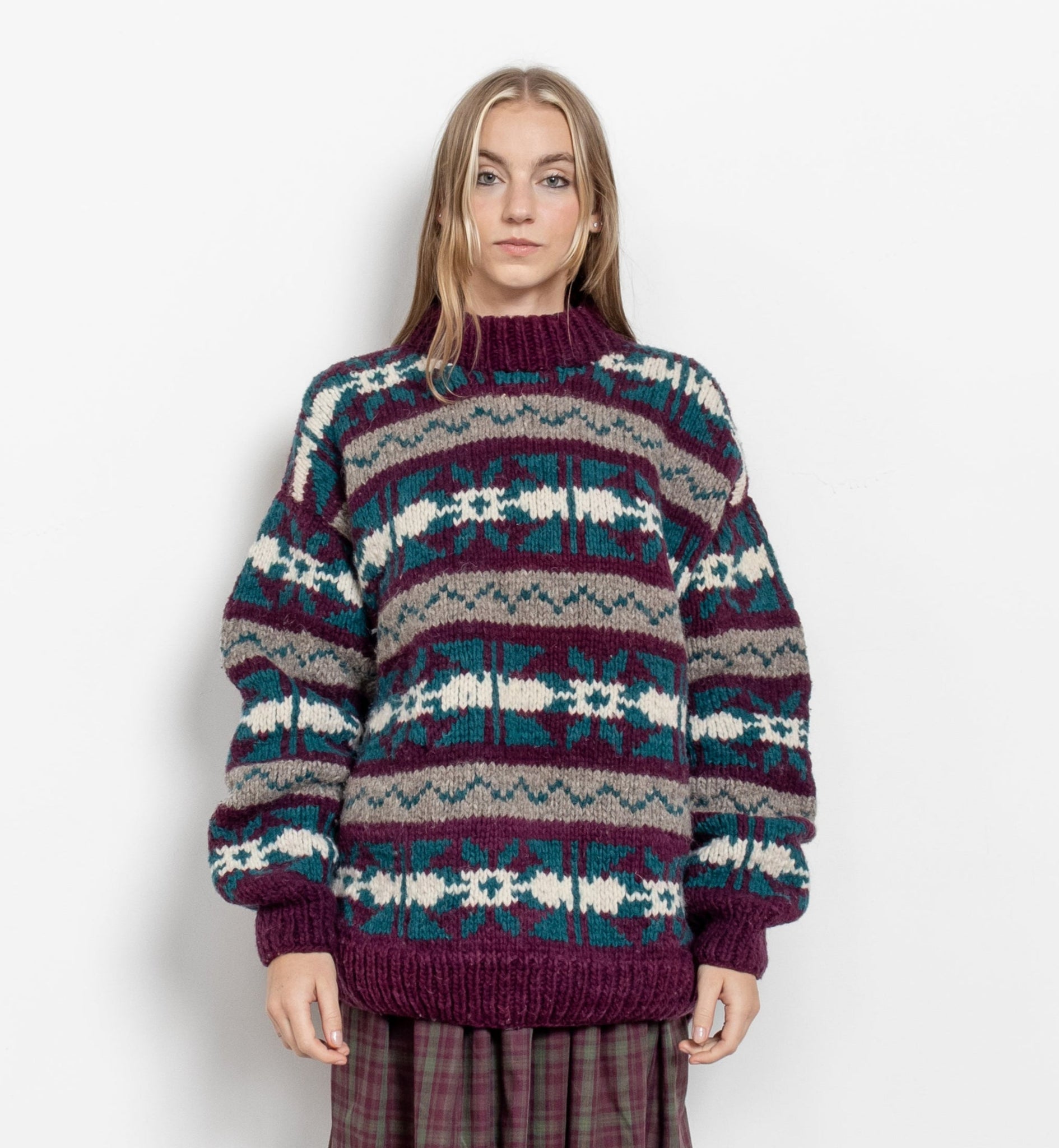 A model wearing a vintage 90's chunky hand knit oversize sweater with a geometric fair isle pattern in burgundy, teal, and grey.