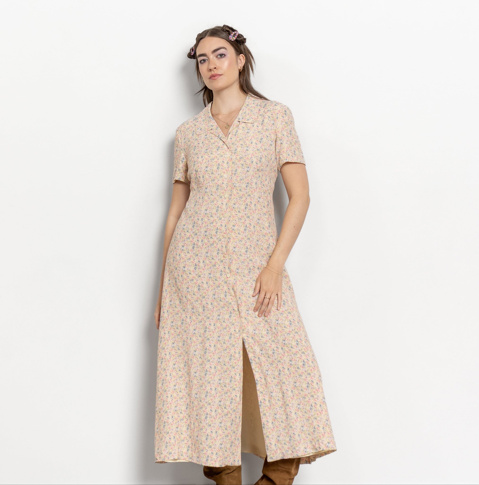 Woman wearing a beige floral dress with brown boots on a white background