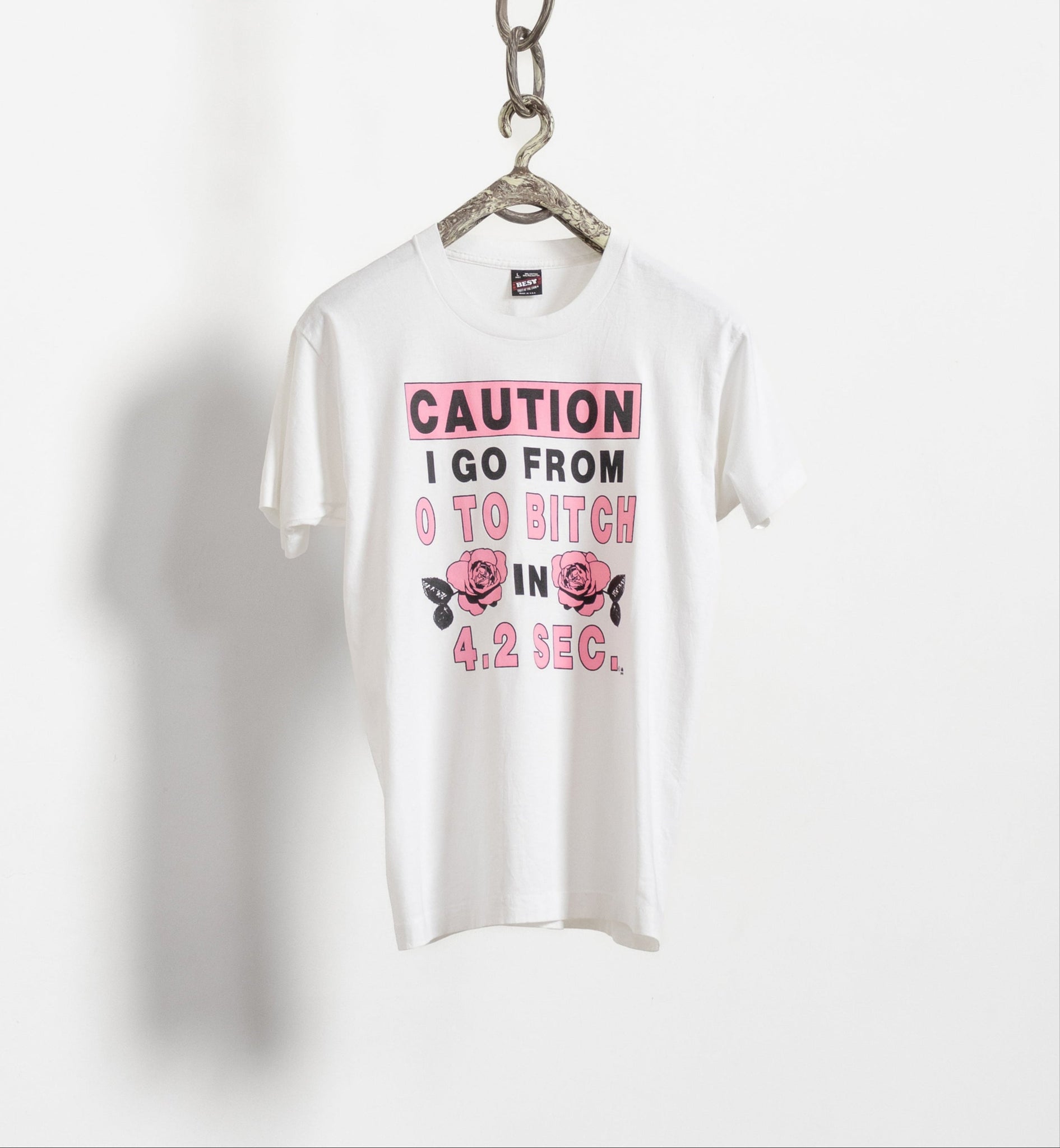 A white short-sleeve crew neck t-shirt with text graphic hanging on a wall chain.