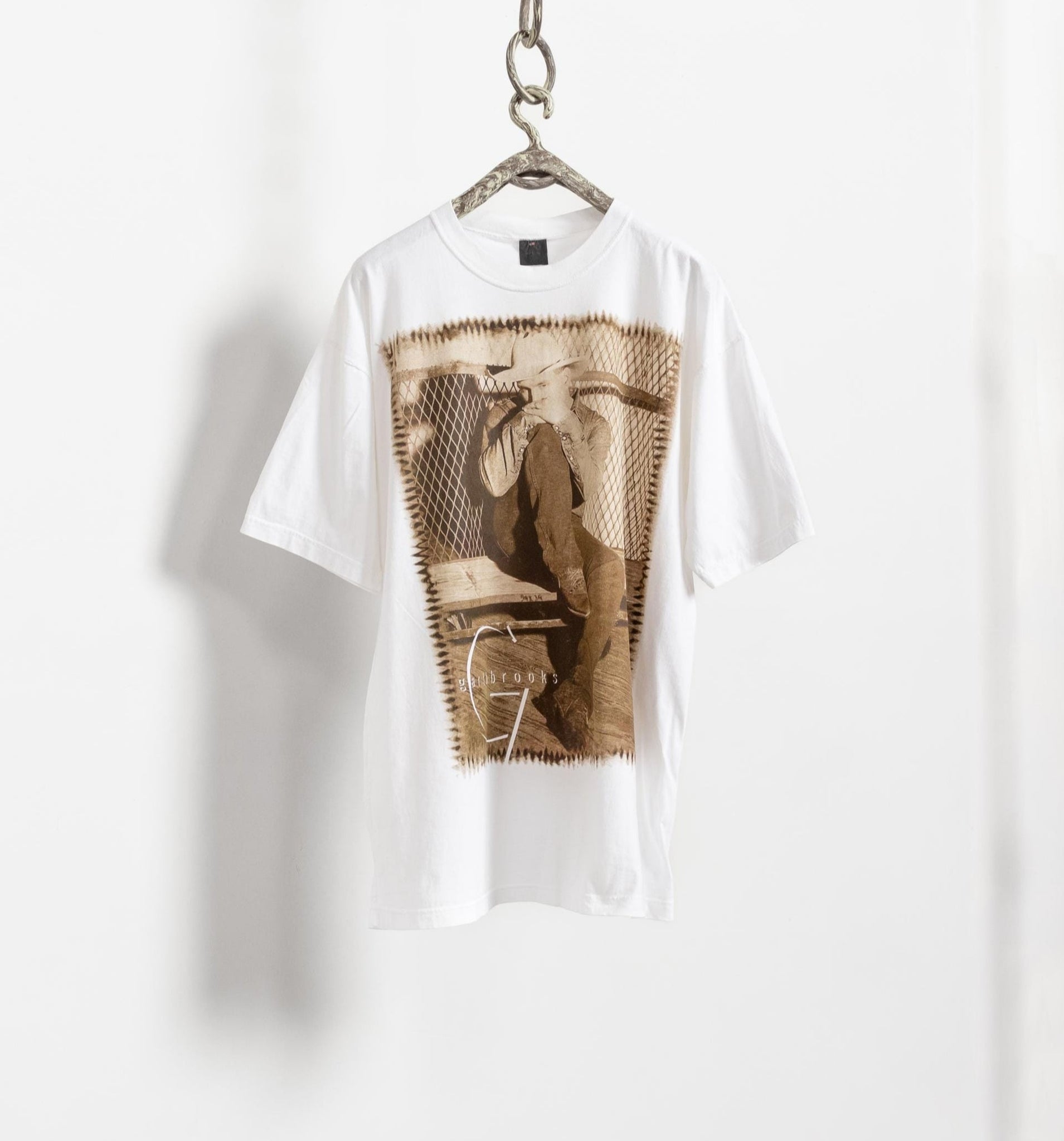 Vintage 80's cotton oversize Garth Brooks graphic tee hanging on a hanger against a white wall, with the image of the shirt visible in the foreground.