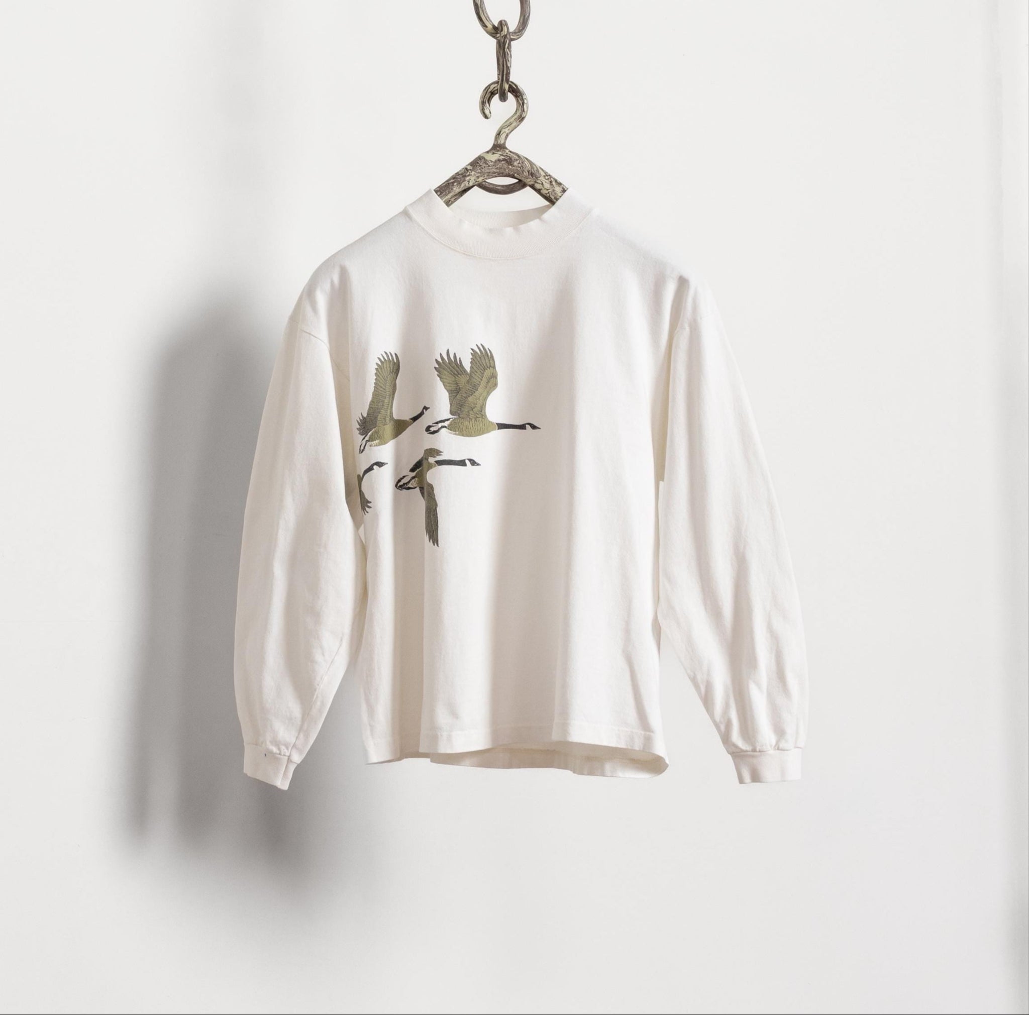 White long-sleeve shirt with bird design on a hanger against a white background