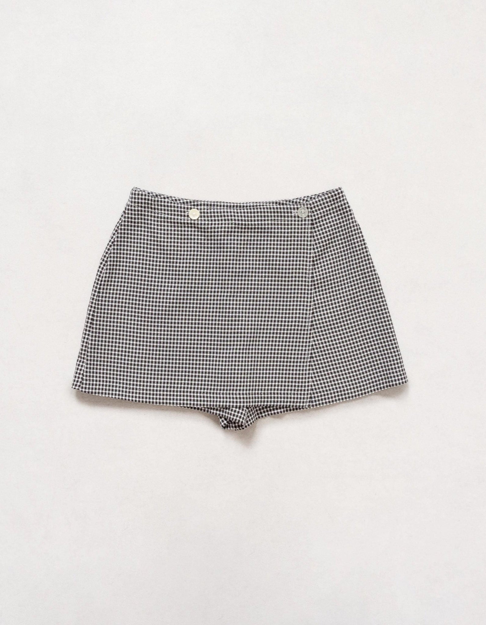 A vintage black and white gingham skort with a high-waisted design, buttons at the side, and a skirt flap over the front.
