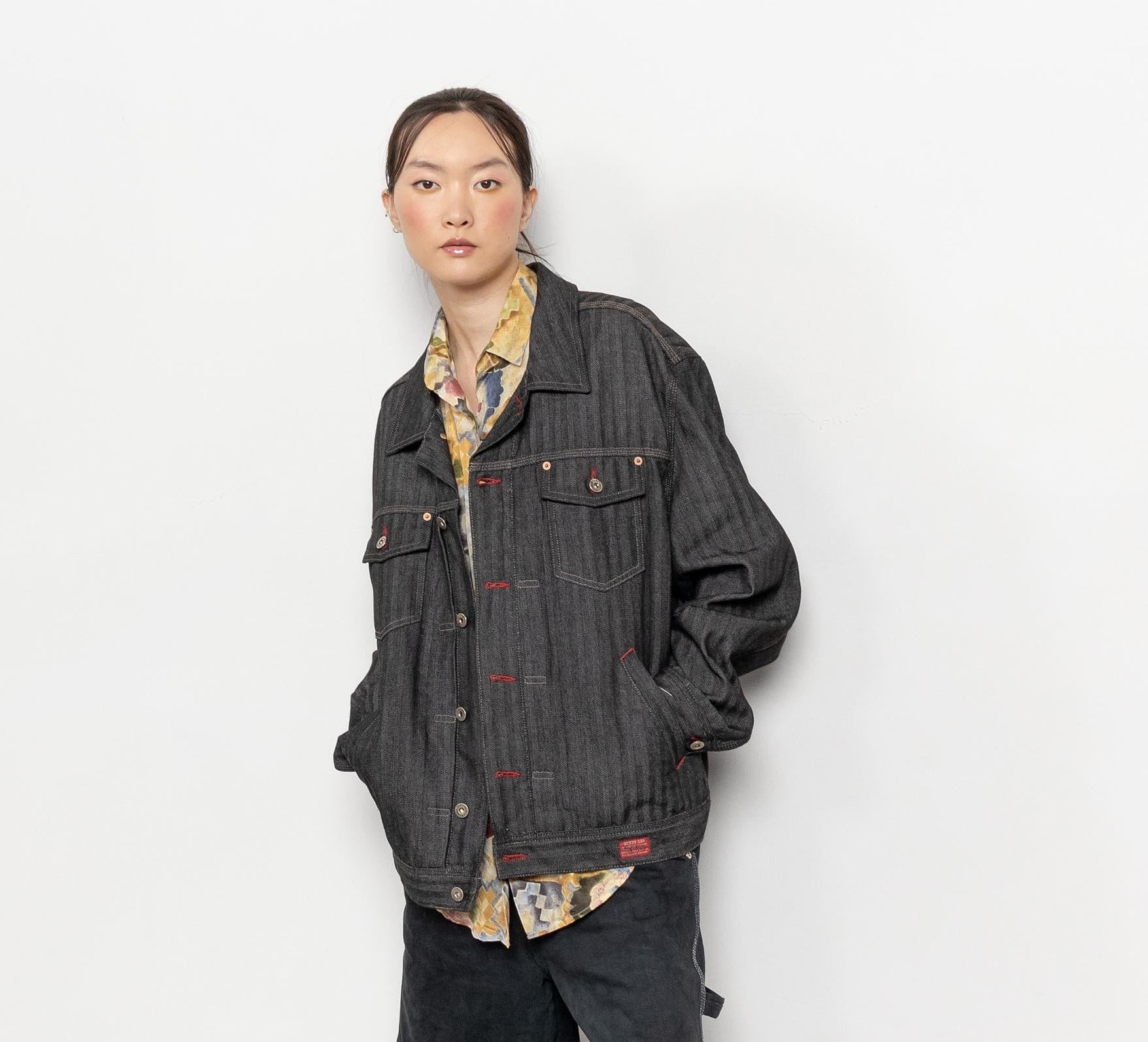 Person wearing a dark denim jacket over a patterned shirt on a white background