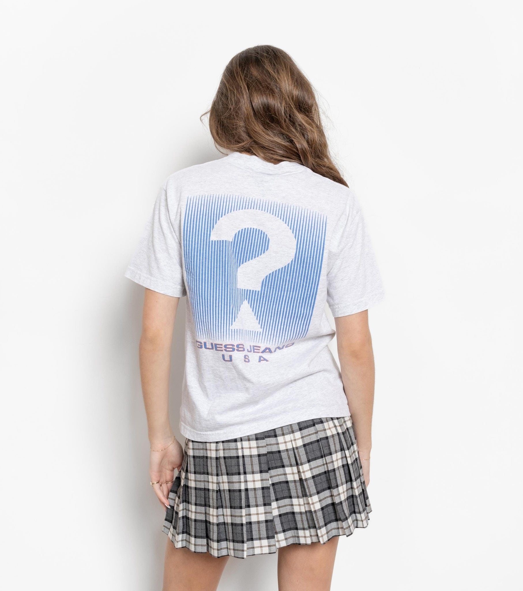 A person wearing a white t-shirt with a large question mark graphic in blue and red, and a plaid skirt.