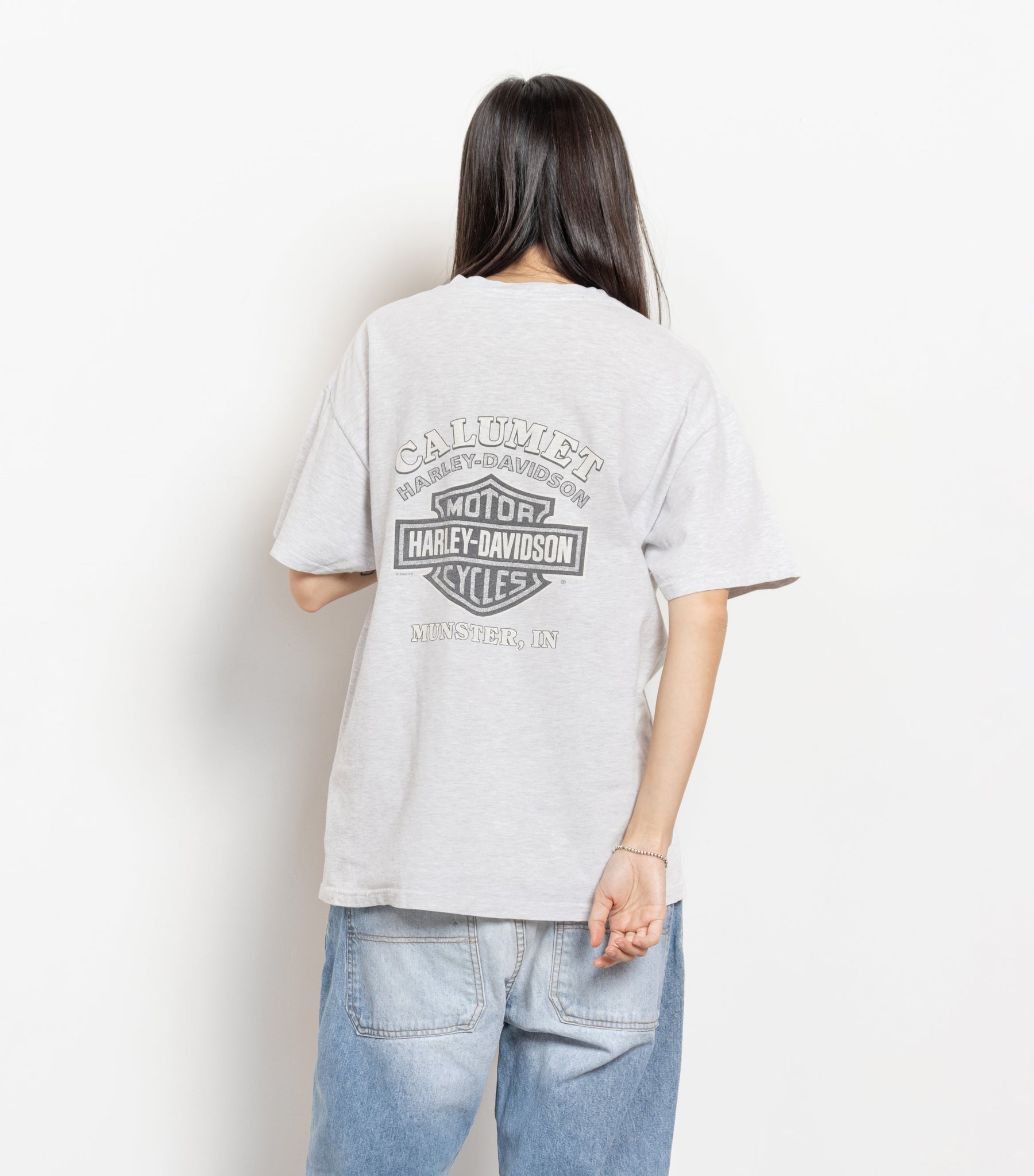 A person wearing a white Harley Davidson graphic t-shirt with the classic Harley logo on the back, and a smaller front pocket logo. The person is facing away from the camera, providing a back view of the t-shirt.