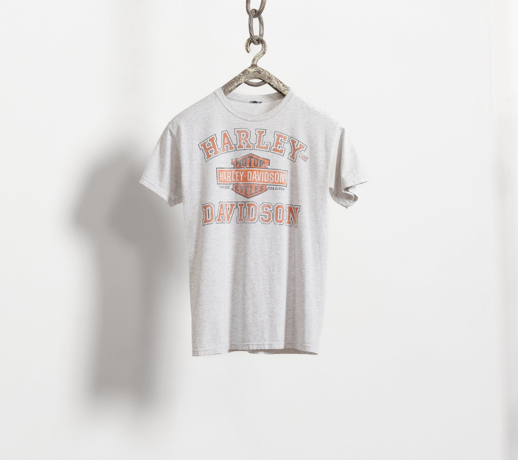 A vintage white Harley Davidson t-shirt with the brand's logo in orange and black on the front, and a graphic on the back.