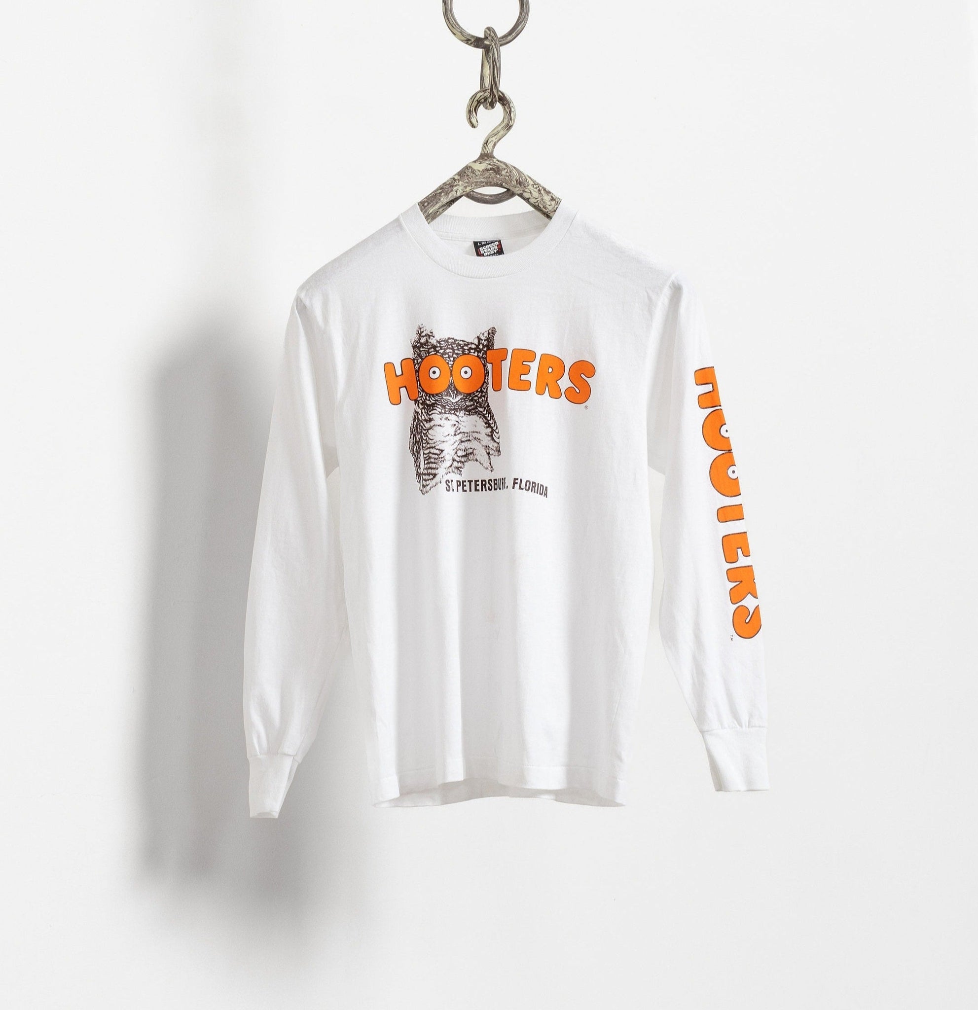 White long-sleeve shirt with 'Hooters' logo and design on a hanger against a white background