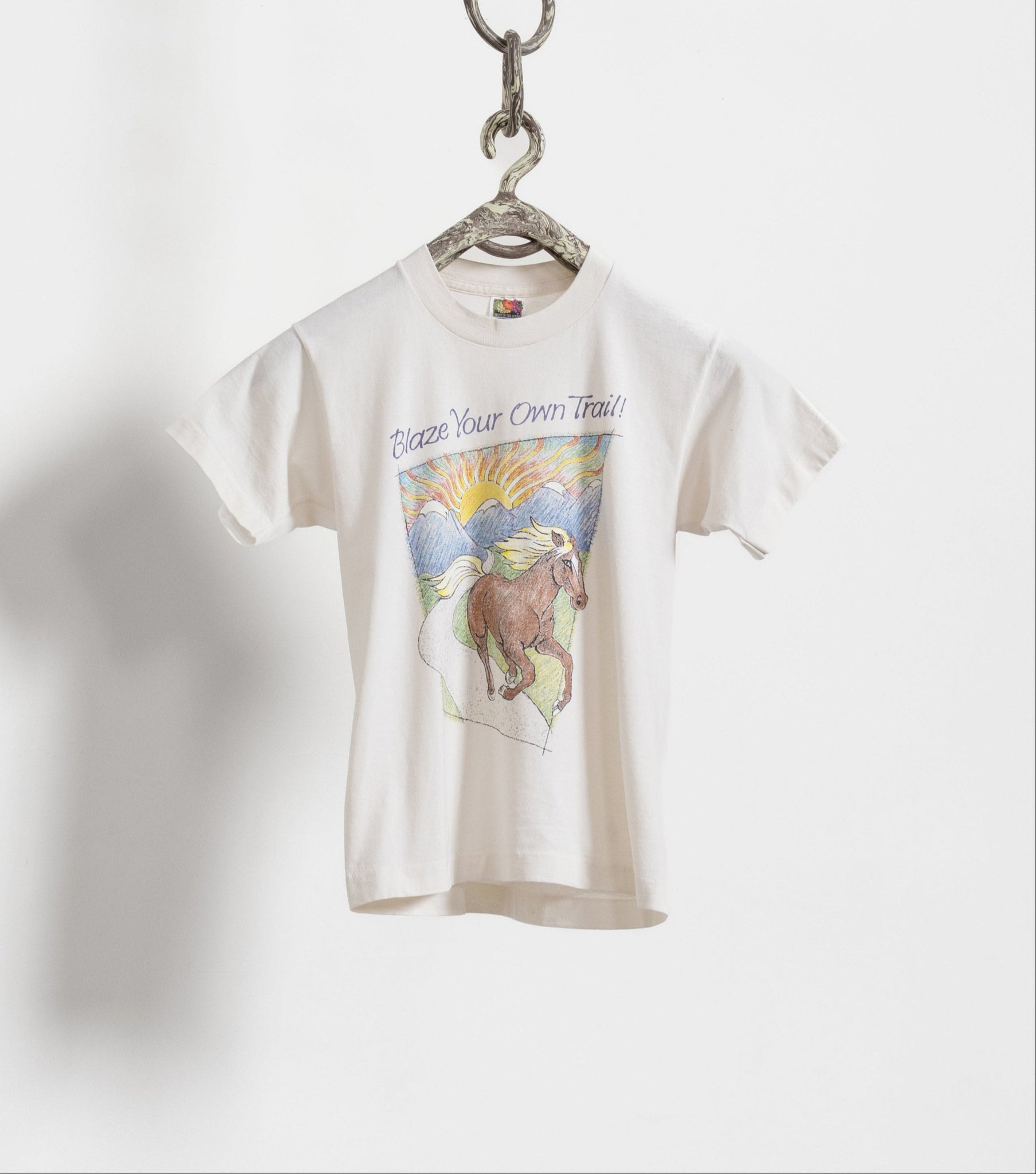 A white vintage t-shirt with a horse graphic, hung on a hanger against a white background.