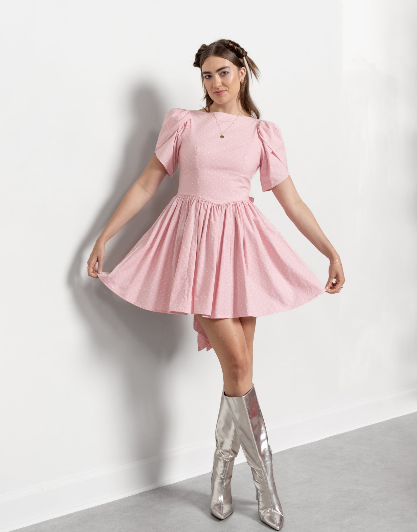 Woman wearing a pink dress with puffed sleeves and silver high-heeled boots on a white background