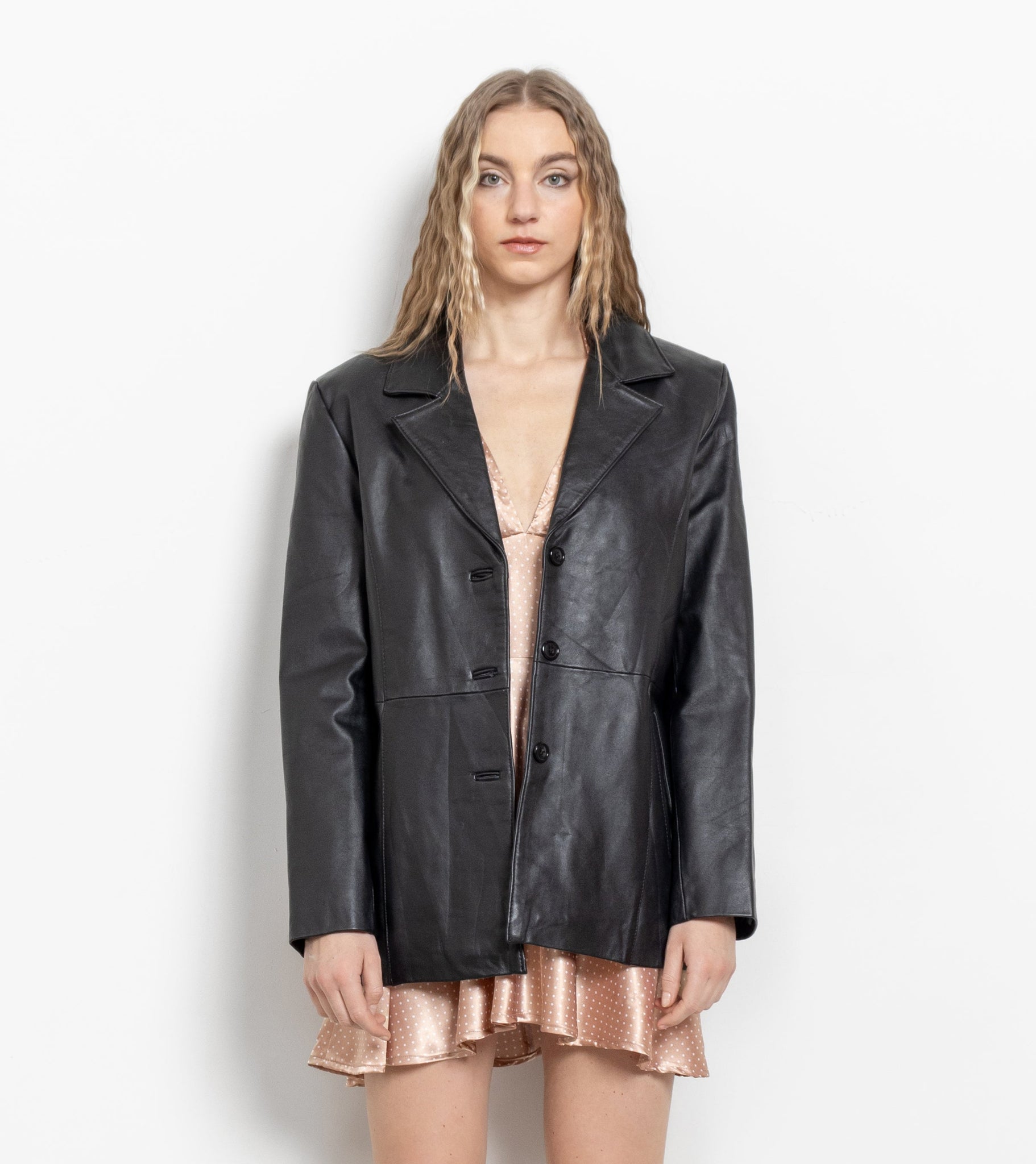 Woman wearing a black leather jacket, bronze skirt, and white knee-high boots on a white background