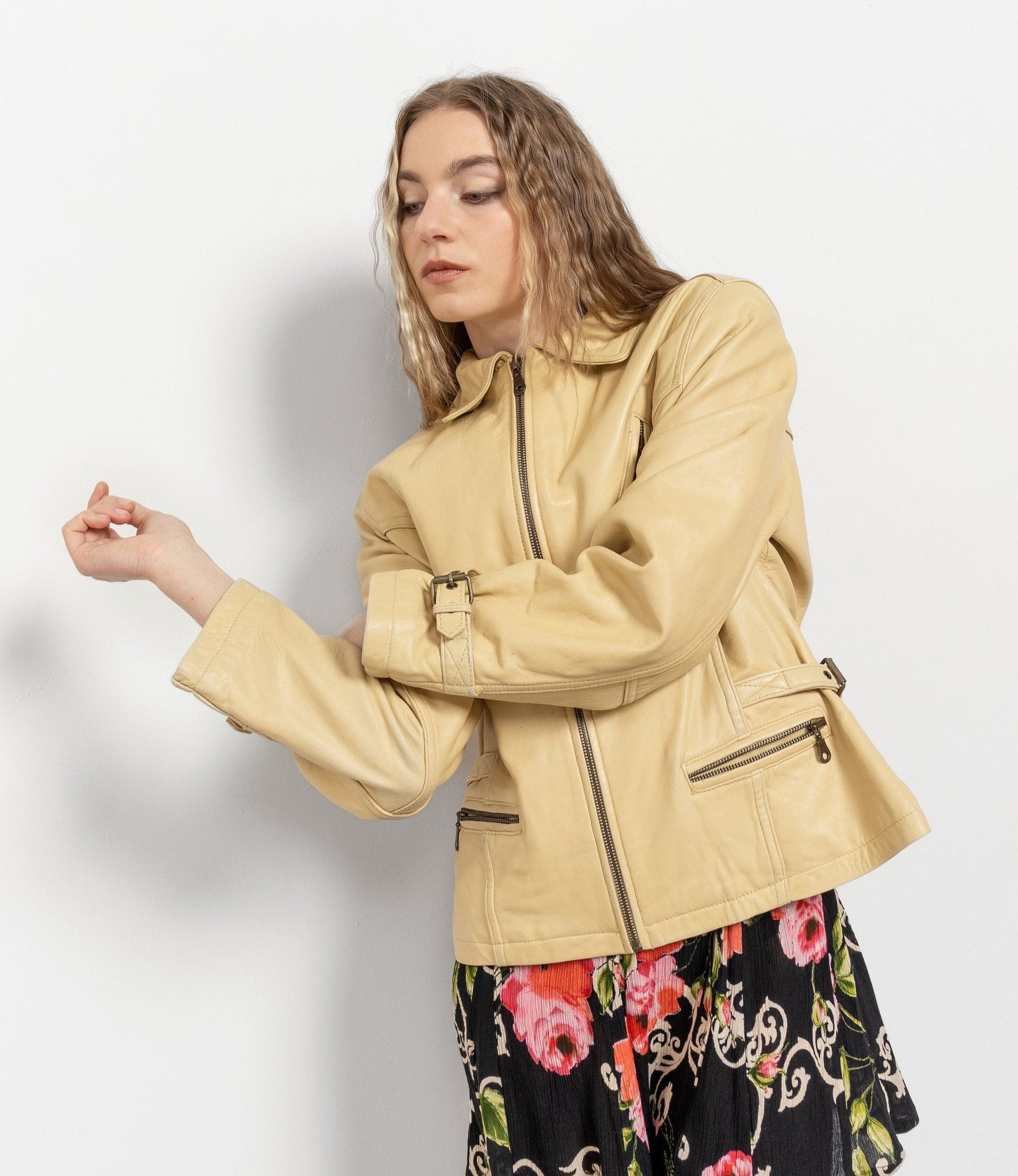 Woman wearing a beige jacket with a floral dress underneath on a white background