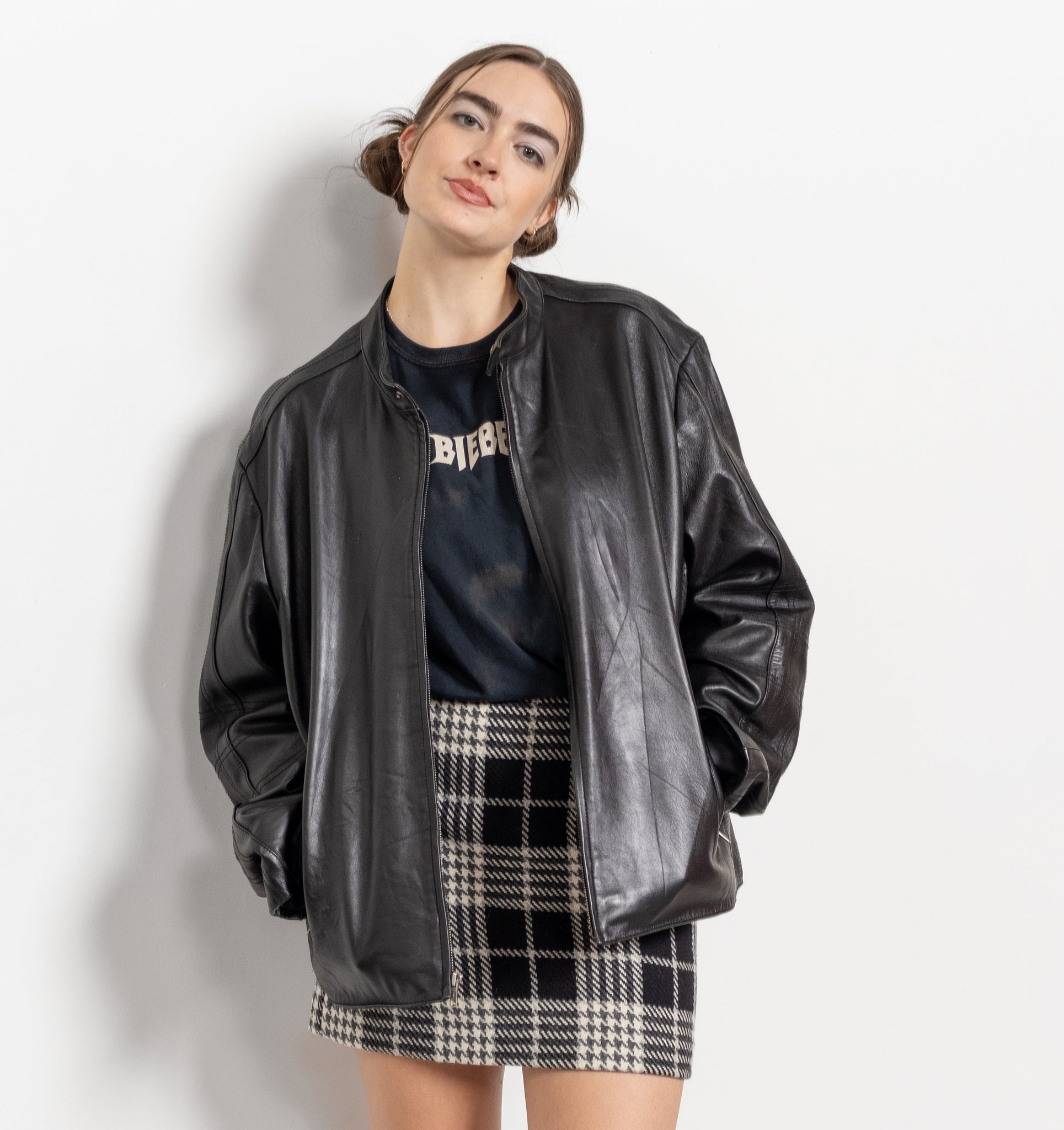 Person wearing a black leather jacket, black t-shirt, plaid skirt, and black boots on a white background