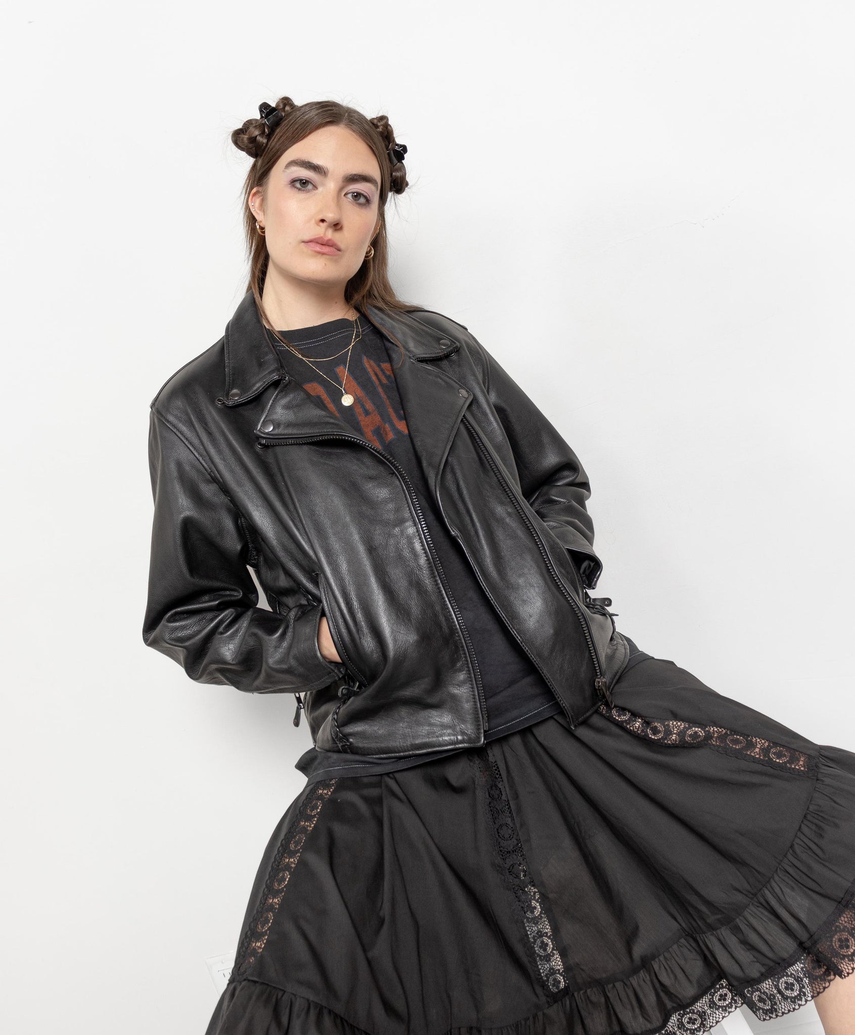 Person wearing a black leather jacket and black dress with lace details on a white background