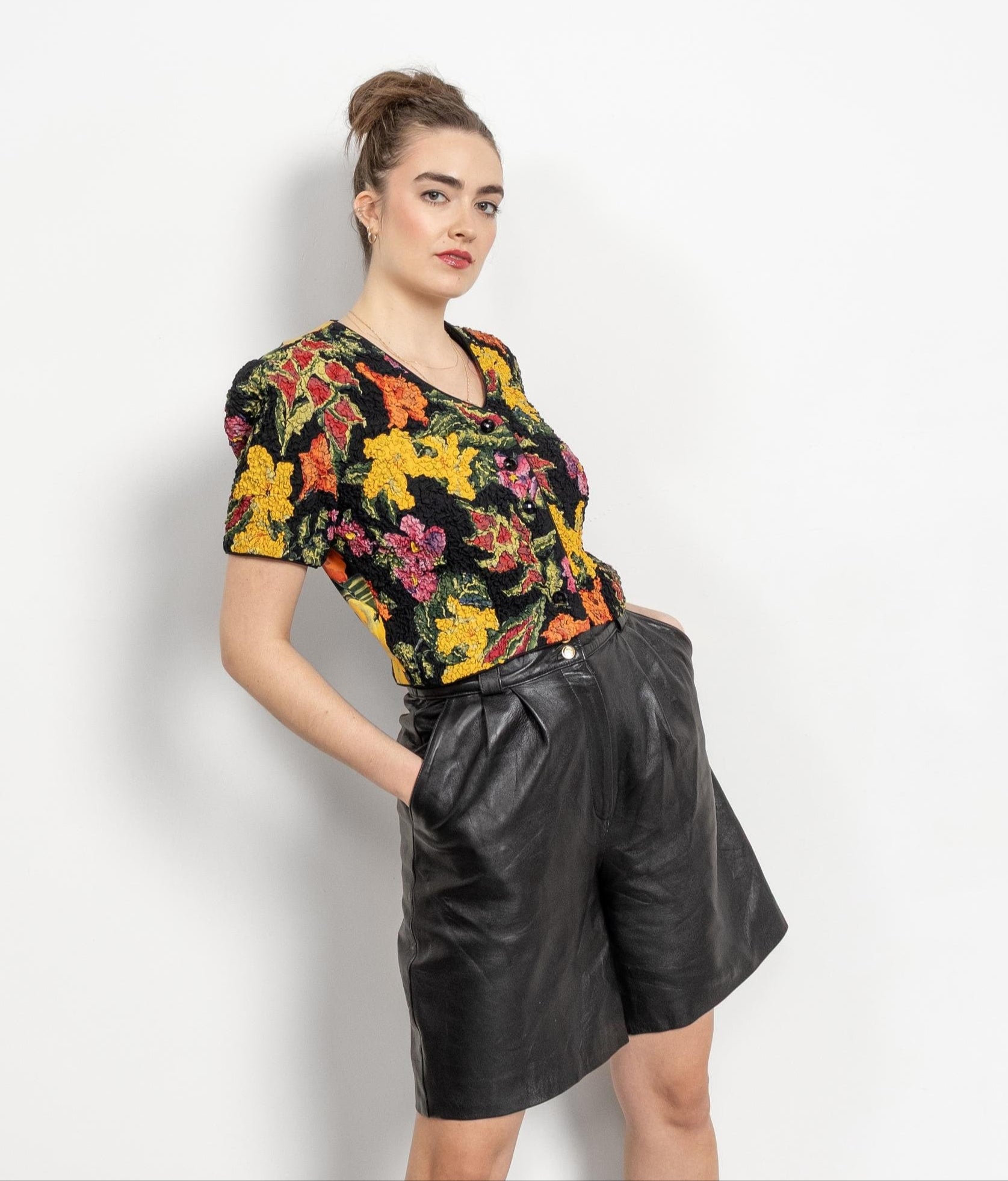 Woman wearing a floral top and black leather shorts against a white background