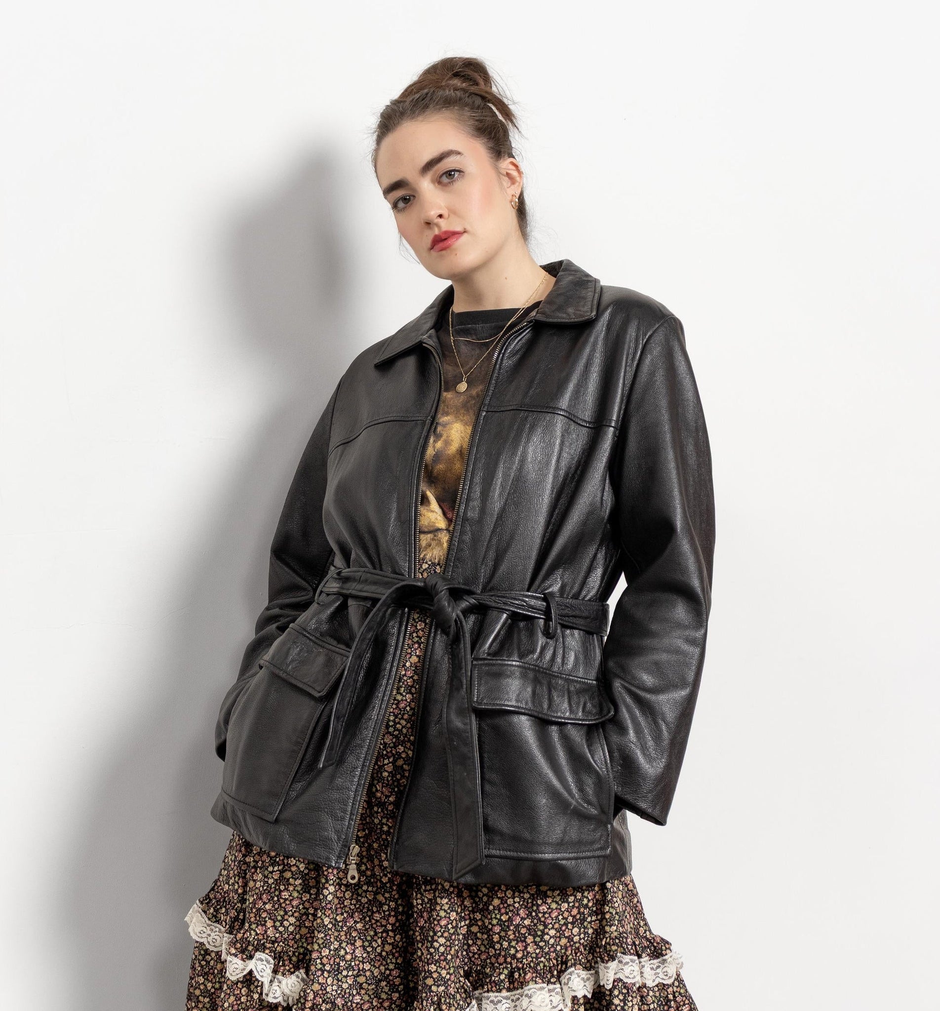 Woman wearing a black leather jacket over a patterned dress on a plain background